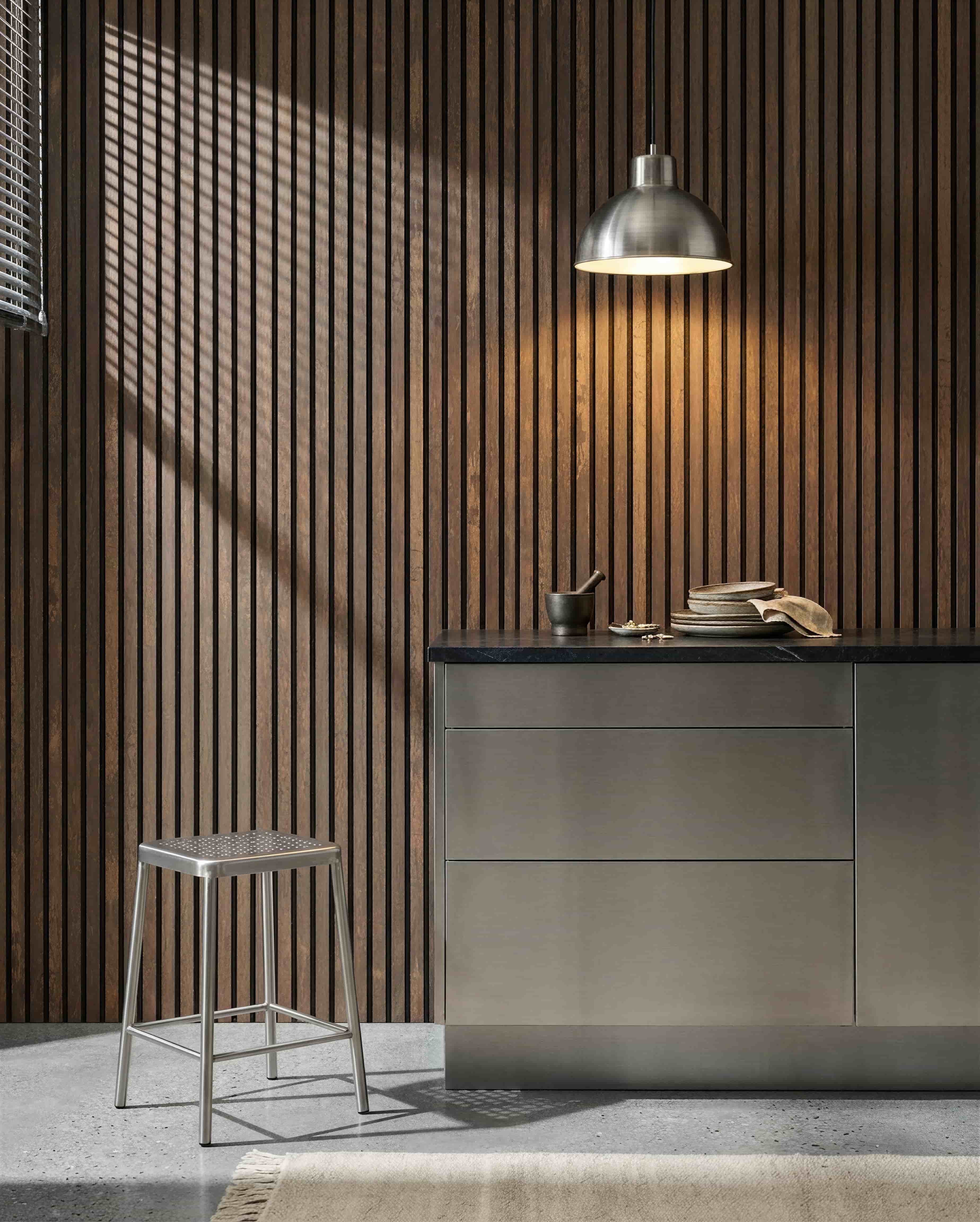 Keuken met een WoodUpp Akupanel Oxide Copper akoestische lattenwand, een roestvrijstalen werkblad, metalen kruk, hanglamp, verschillende schalen en een vijzel.