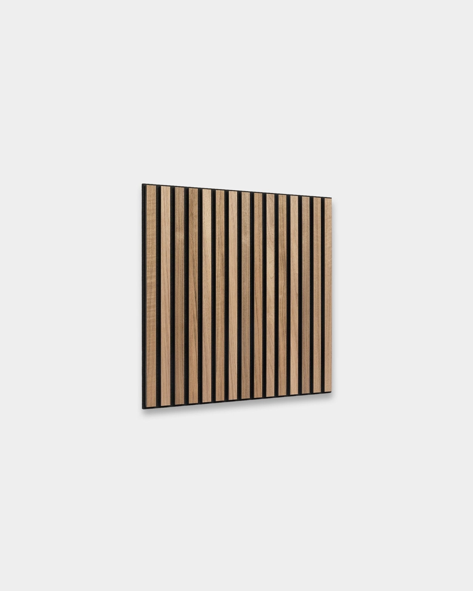 WoodUpp Akupixel Akoestisch paneel in walnoot, 60x60 cm, heeft gelijkmatig verdeelde walnoothouten latten met black tussenruimtes, gemonteerd op een lichtgrijze muur voor een Scandinavische uitstraling.