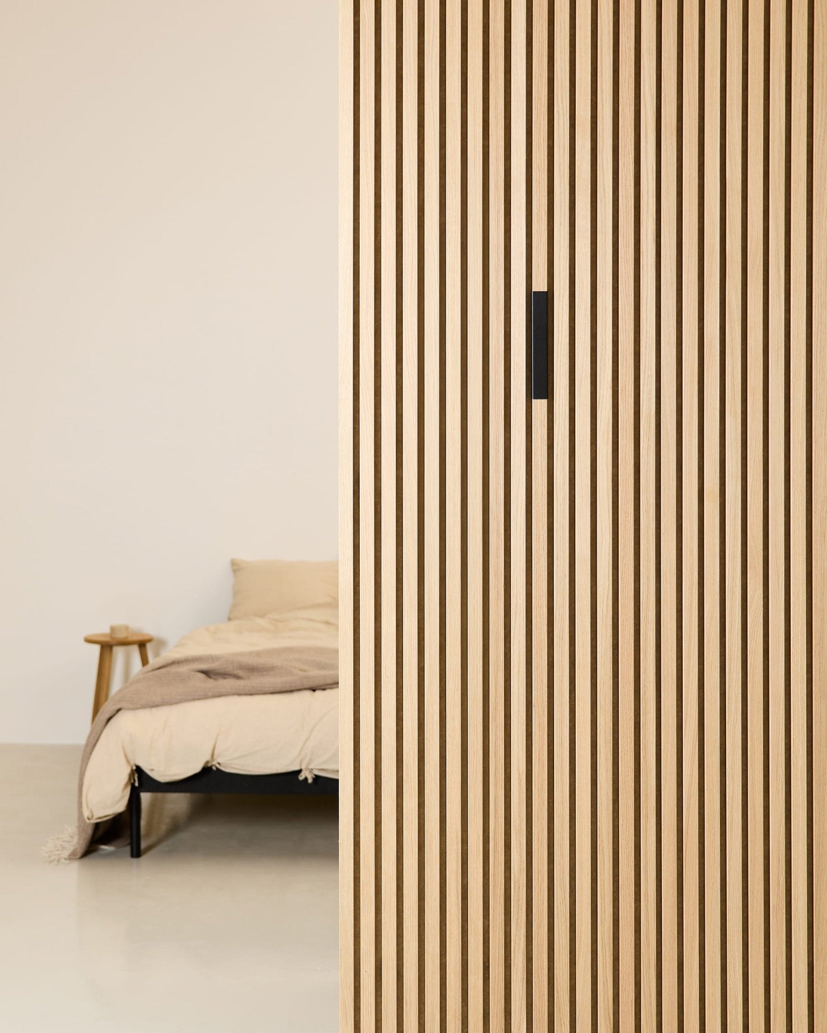 Minimalistische slaapkamer met een beige bed, een houten bijzettafeltje en een WoodUpp Liva Black Aluminium akoestisch paneel dat textuur toevoegt aan de verticale scheidingswand.