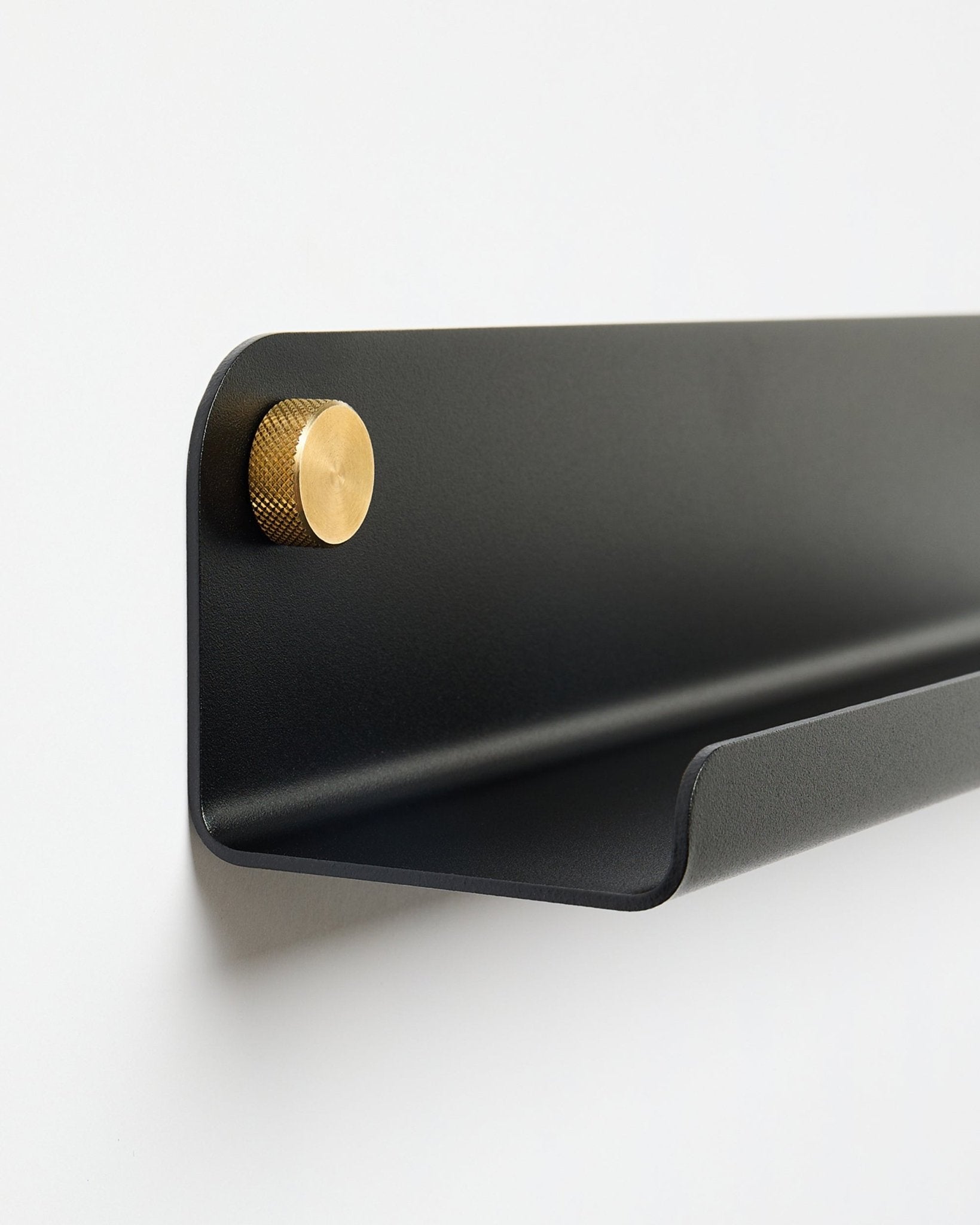 De Norr | Narrow Shelf in black (115,9 cm) met links één gouden knop, van WoodUpp, gemonteerd op een effen witte muur.