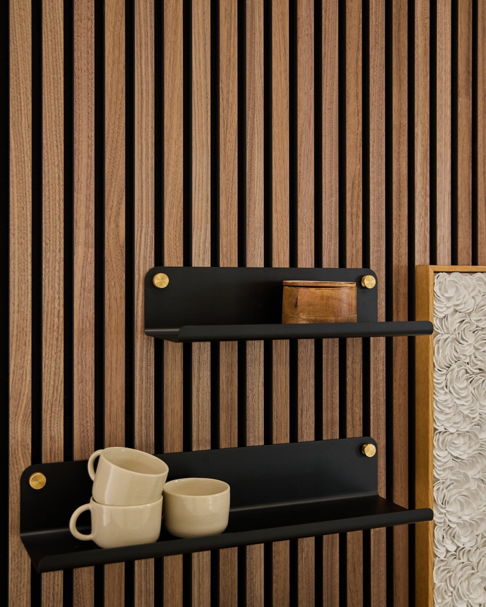 Twee black Norr | Wide Shelves van WoodUpp (35,9 cm) met gouden beugels, gemonteerd op een Akupanel akoestisch houten paneel; op de onderste plank staan 3 beige mokken, op de bovenste staat een small houten doos.