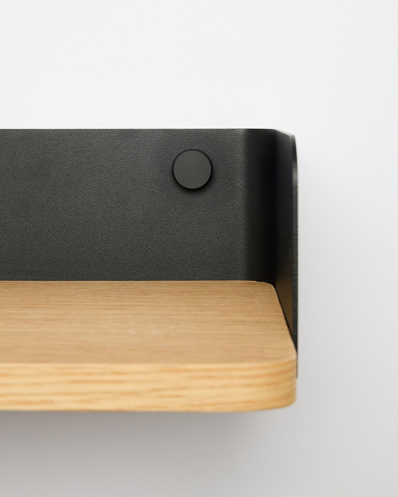 Linn boekenkast van WoodUpp in natural oak, 55,9 cm breed, met black metalen beugel, gemonteerd aan een witte muur; close-up van de rechterkant.