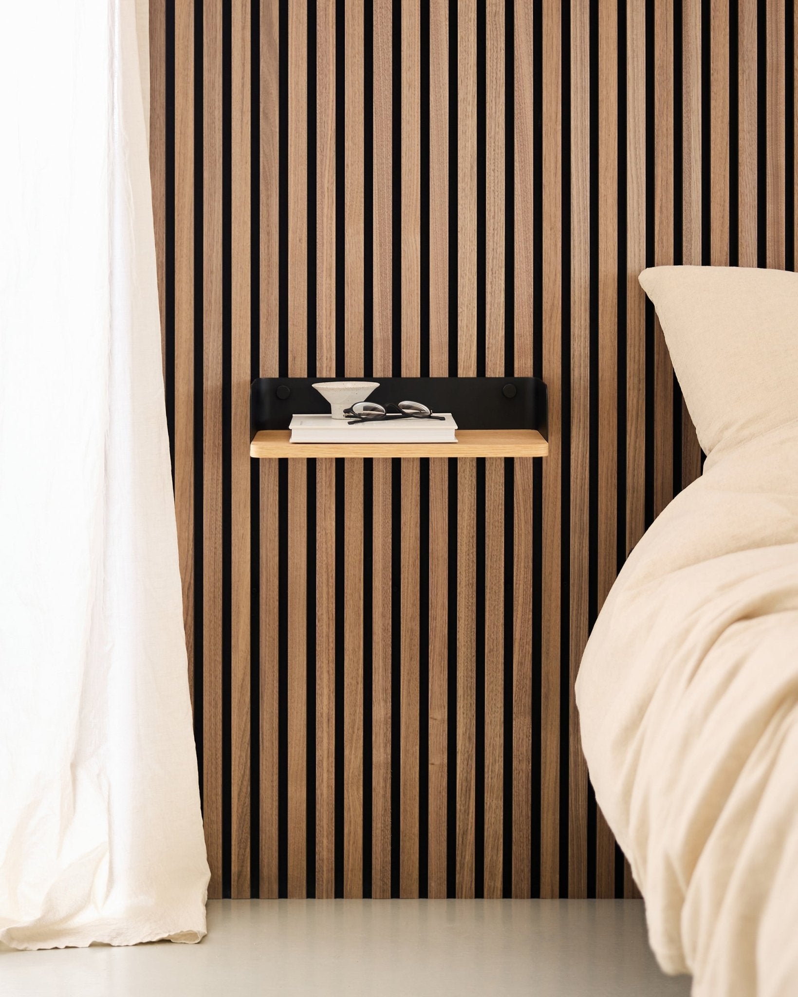 Minimalistische slaapkamer met een Scandinavische houten lattenwand Akoestisch paneel, de WoodUpp Linn boekenplank in Natural Oak, en een zwevend nachtkastje naast een beige bed.