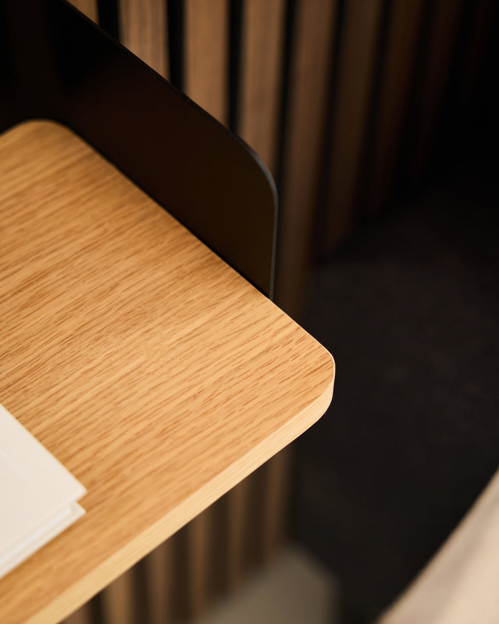 Close-up van een bureauhoek met black Akupanel akoestische houten panelen, witte papieren en de WoodUpp Linn boekenplank in Natural Oak (39,9 cm) op de achtergrond.
