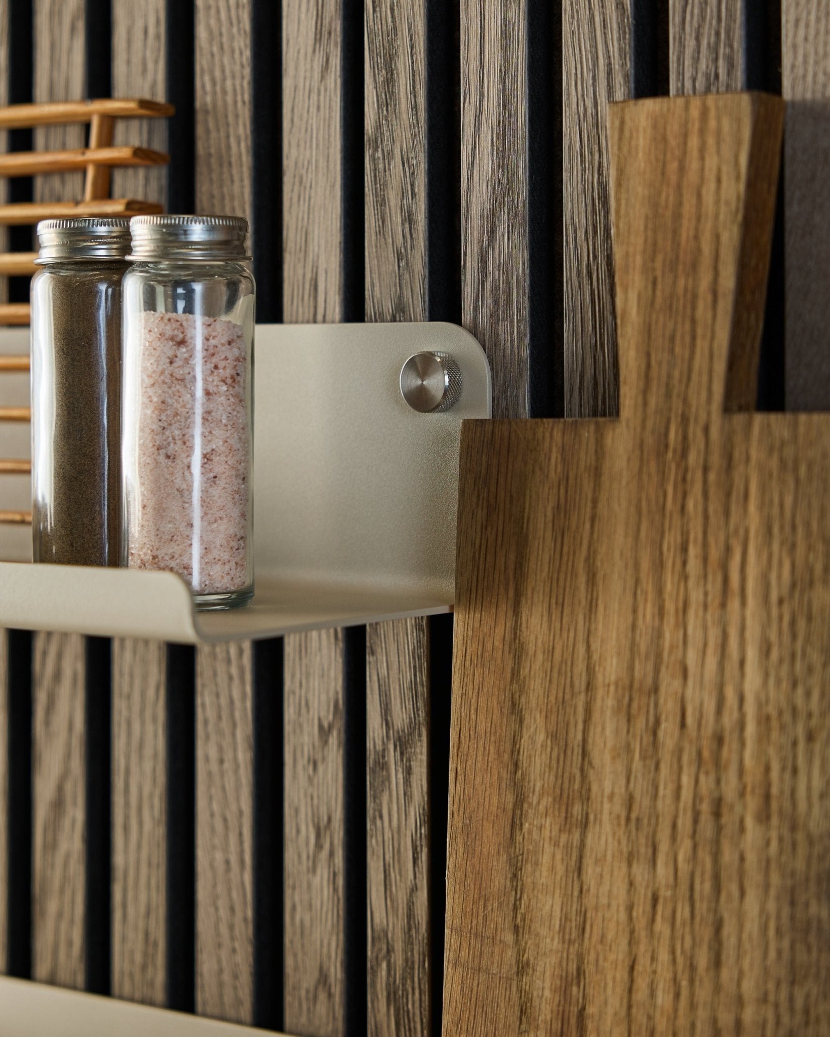 Glazen potten met kruiden en een houten snijplank staan op de WoodUpp Norr Wide Shelf in beige, 35,9 cm, gemonteerd tegen een vertical akoestisch lattenwandpaneel.