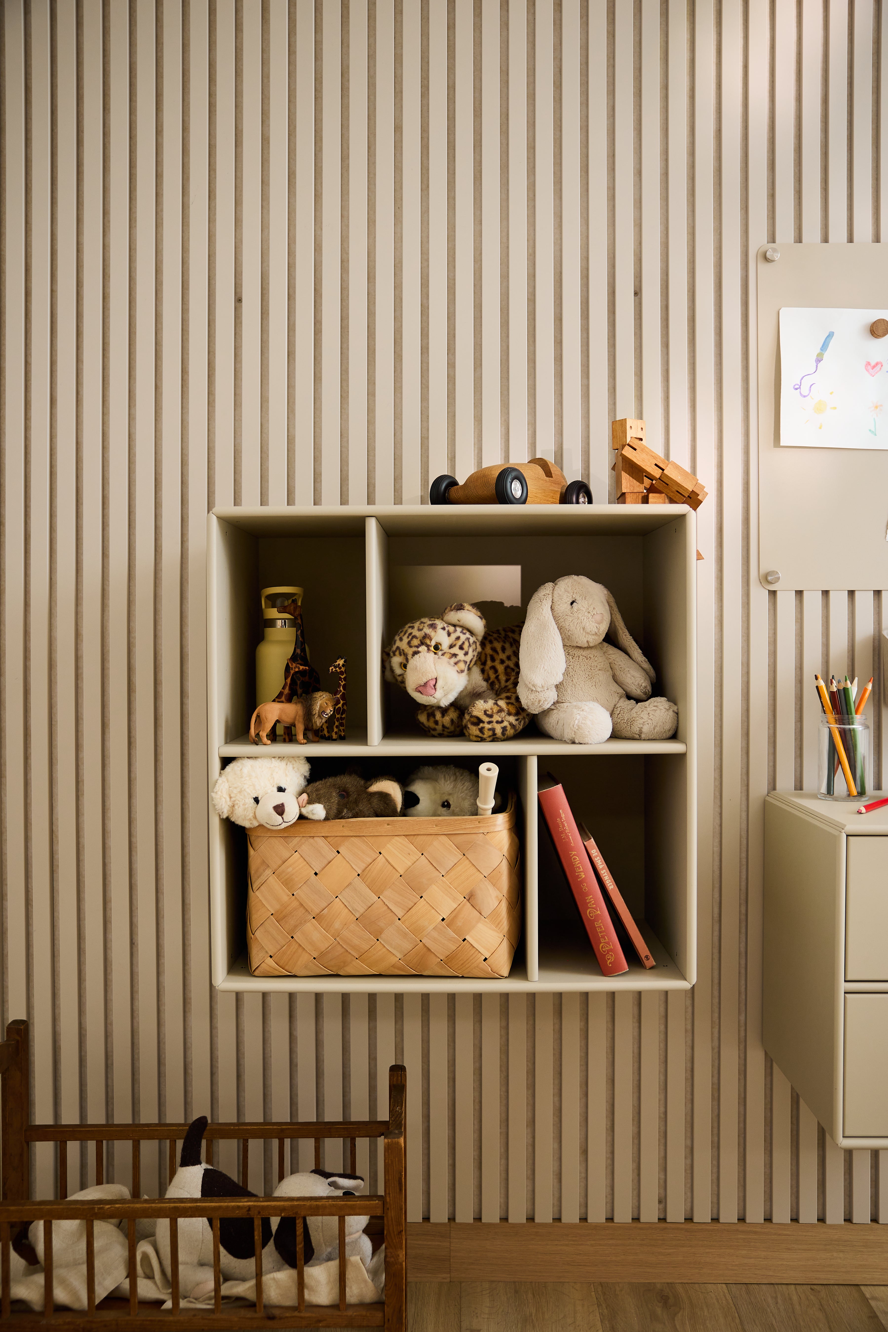 De WoodUpp Arka open kast in beige, gevuld met speelgoed en boeken, tegen een gestreept behang in een kinderkamer, is een toonbeeld van minimalistisch Scandinavisch design.