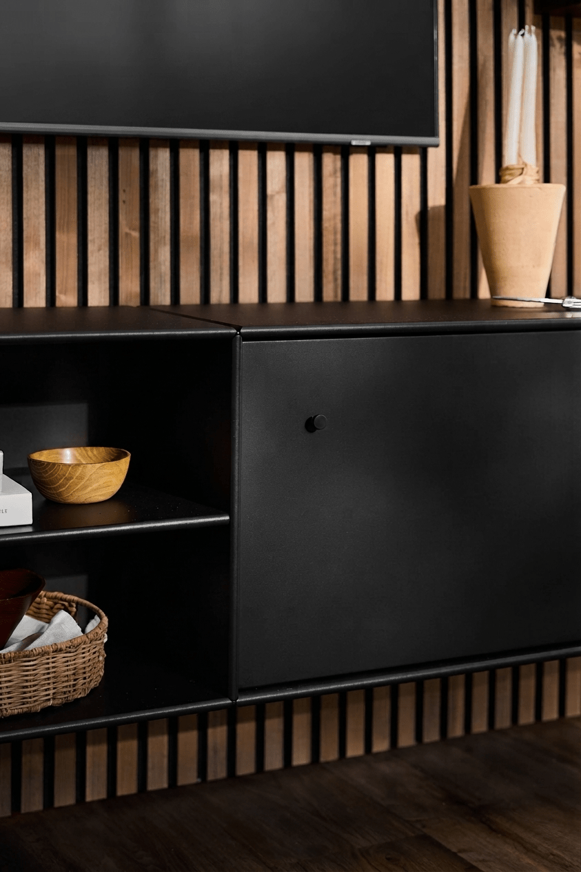 Zwarte WoodUpp Arka tv-kast met open planken voor boeken en manden, een beige vaas, een slimme kabelgeleiding en een verticale Akupanel akoestische houten paneelachtergrond.