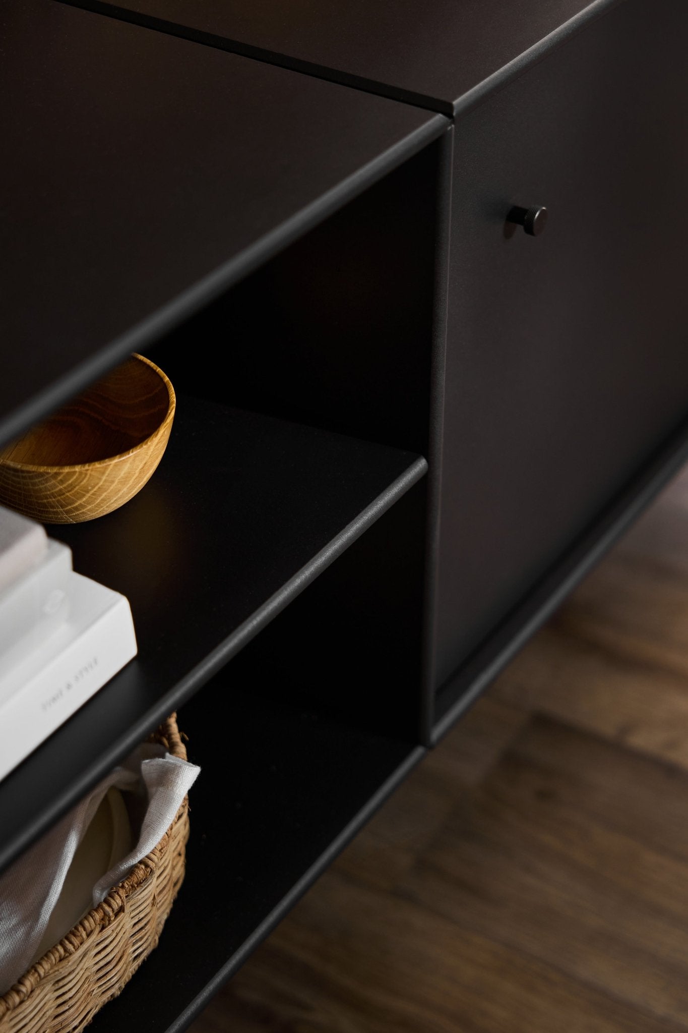 Zwarte Arka-tv-kast van WoodUpp met een minimalistische vormgeving, ontworpen voor kabelbeheer en opbergruimte, geplaatst op een houten vloer.