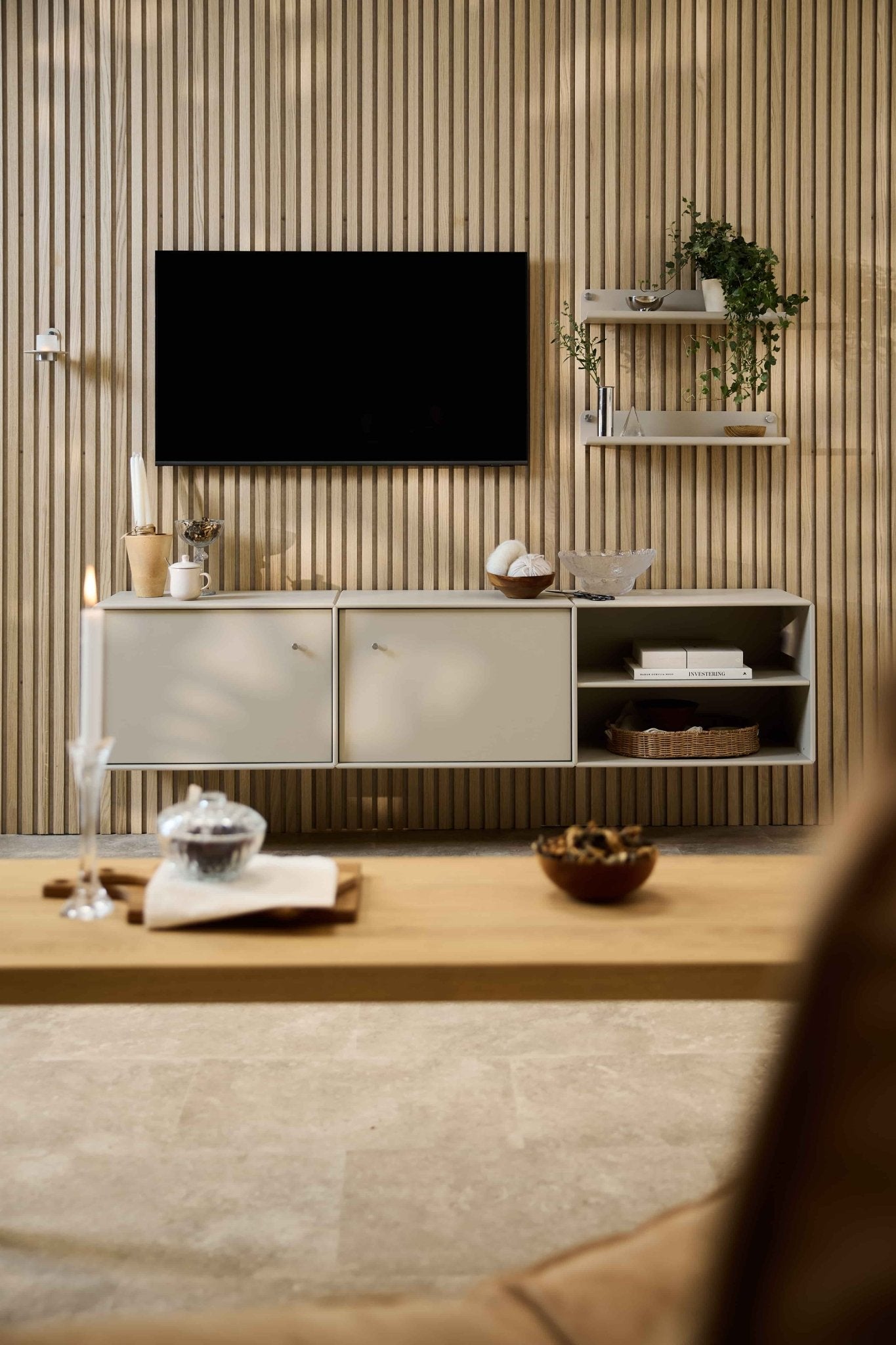 Moderne woonkamer met de Arka-tv-kast van WoodUpp, een modulaire zithoek, Scandinavische planken met planten en decoraties, en een kaars op de salontafel.