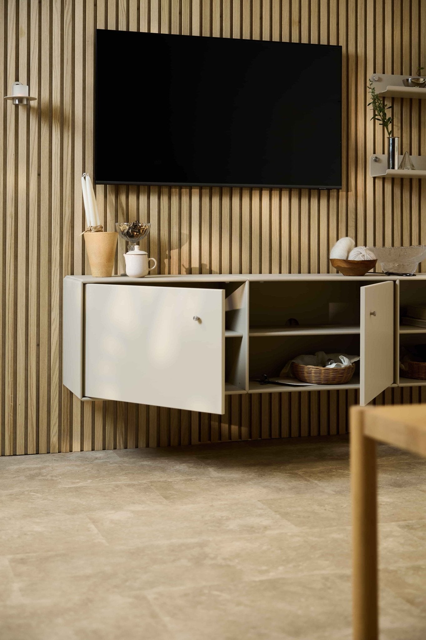 Moderne woonkamer met de Arka-tv-kast in beige van WoodUpp, geplaatst onder een kast en een tv tegen een akoestische houten lamellenwand van Nordic Akupanel. Modulair meubilair.