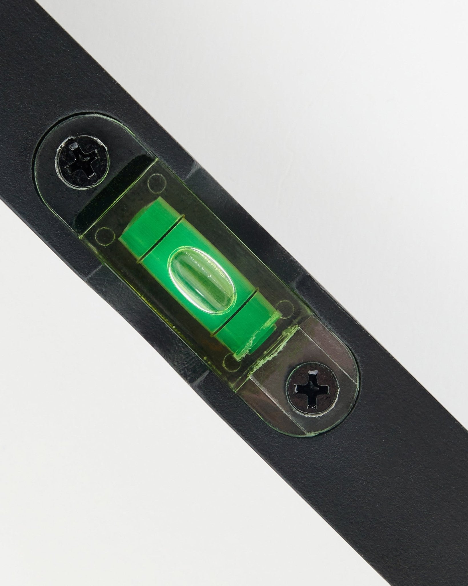 Close-up van een black WoodUpp waterpas (15 x 3,2 cm) met groene libel, gebruikt voor de nauwkeurige montage van akoestische panelen.