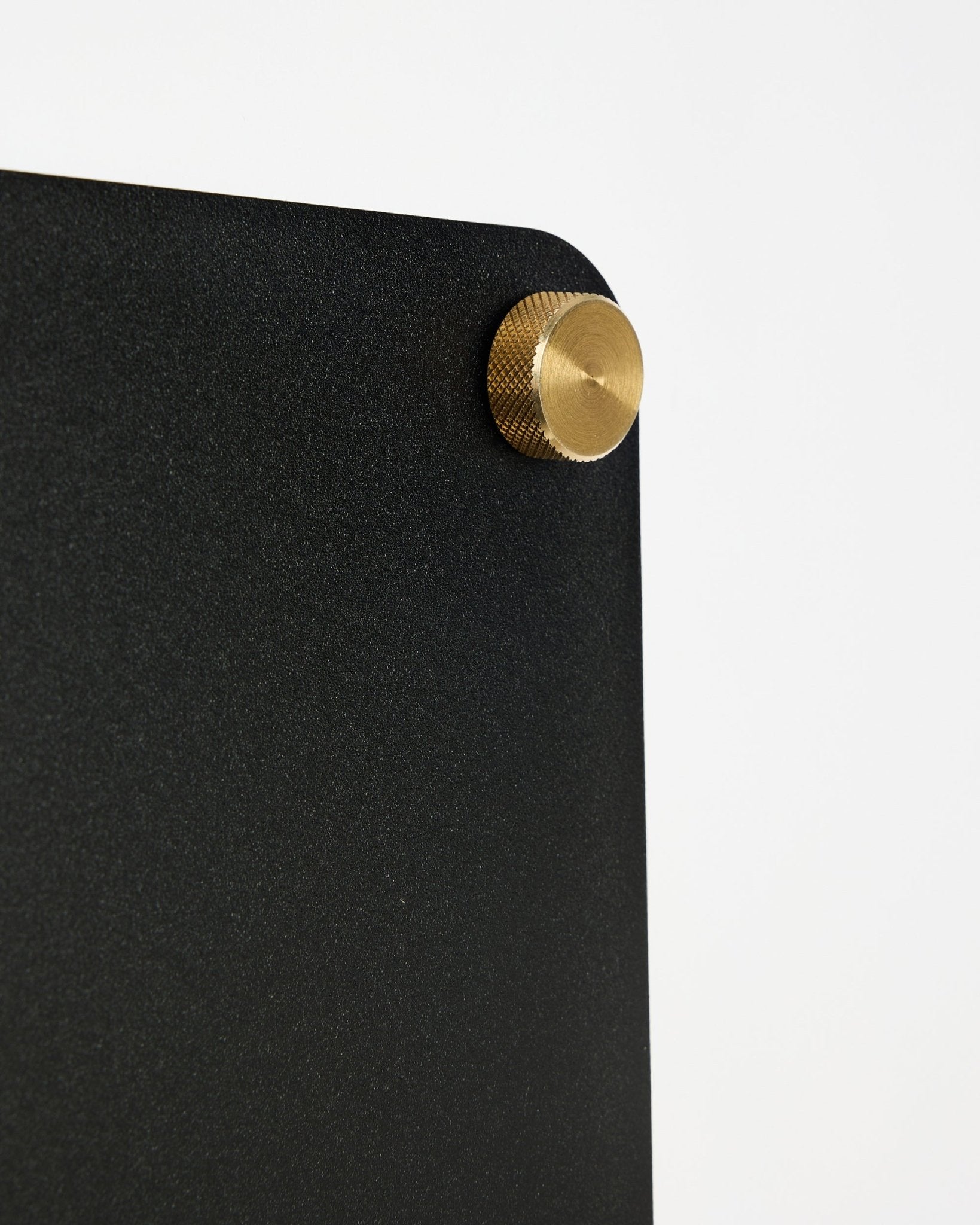 Close-up van WoodUpp Norr black akoestisch magnetisch bord (small) met een afgeronde hoek en gouden schroefbevestiging op een witte achtergrond.