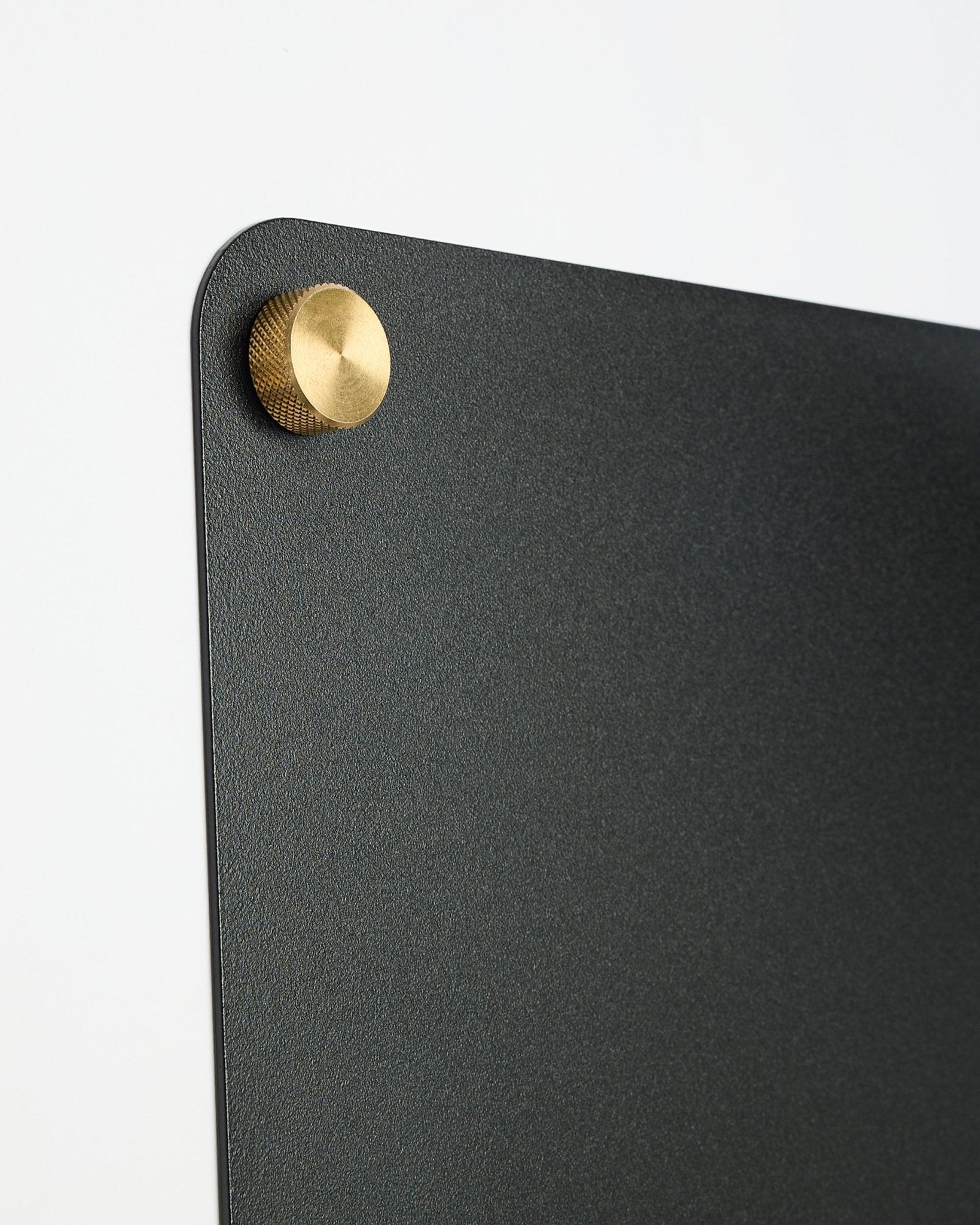 Close-up van een large black Norr magnetisch bord van WoodUpp, onderdeel van de CREATE-collectie, met een ronde goudkleurige metalen bevestiging in de bovenhoek.