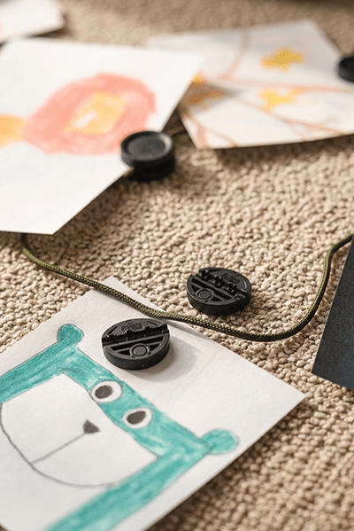 Kindertekeningen hangen met neodymiumclips aan de WoodUpp Vindar | Gallery String; groene berenkunst ligt op beige tapijt onder de Akoestisch paneel.
