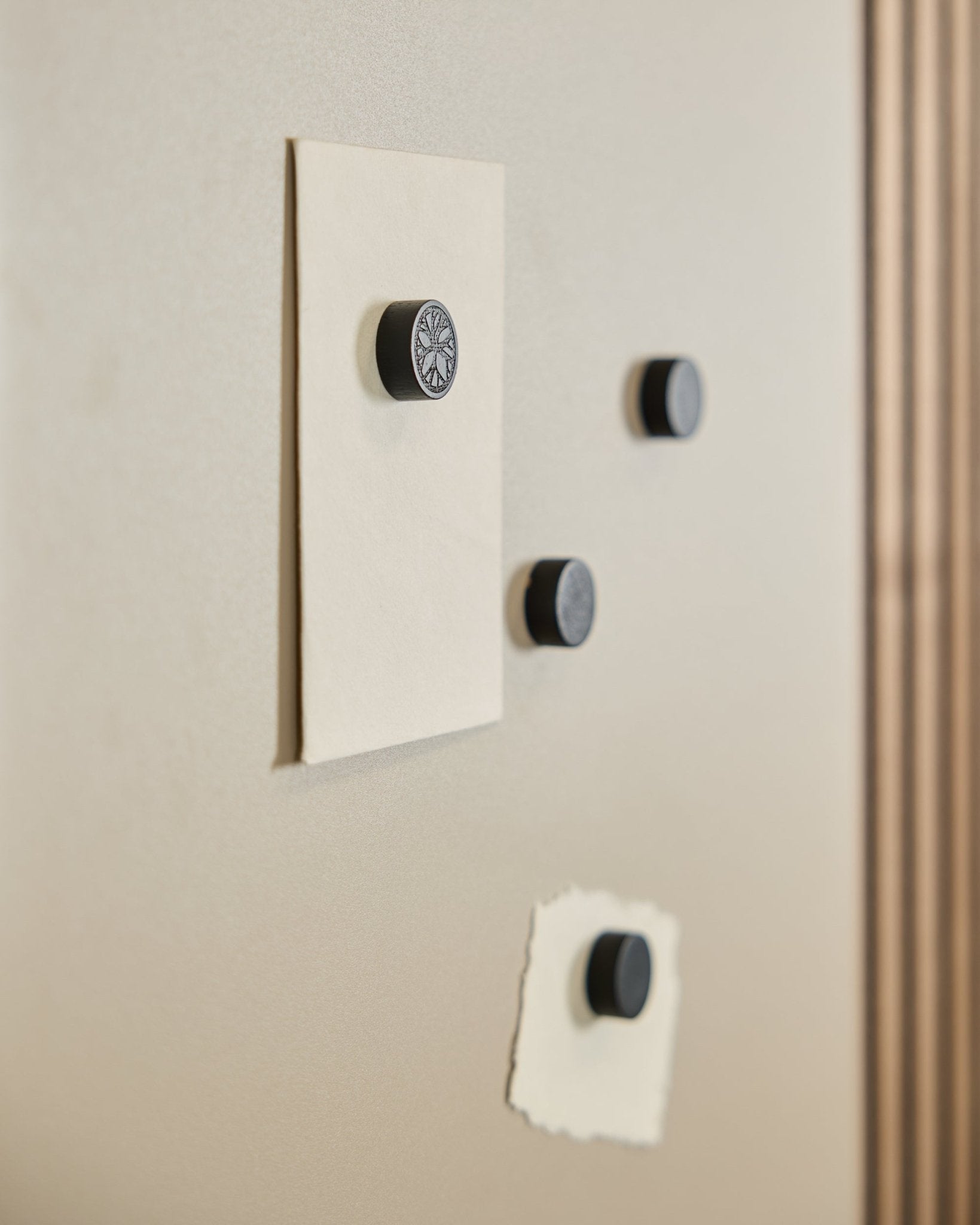 Vier WoodUpp Norr Magnet set in Black Oak (4 stuks) houden twee vellen papier vast op een Norr Magnetic Board, met rechts een deel van een Akoestisch paneel zichtbaar.