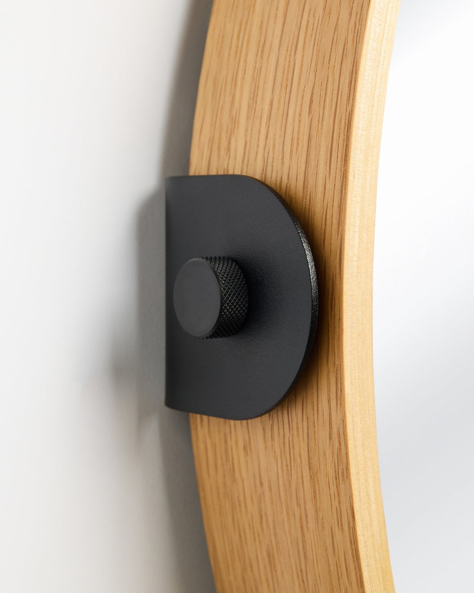 Detail van de WoodUpp Linn Mirror in Natural Oak, een Akoestisch paneel dat met een black metalen beugel en ronde knop aan de muur is gemonteerd.