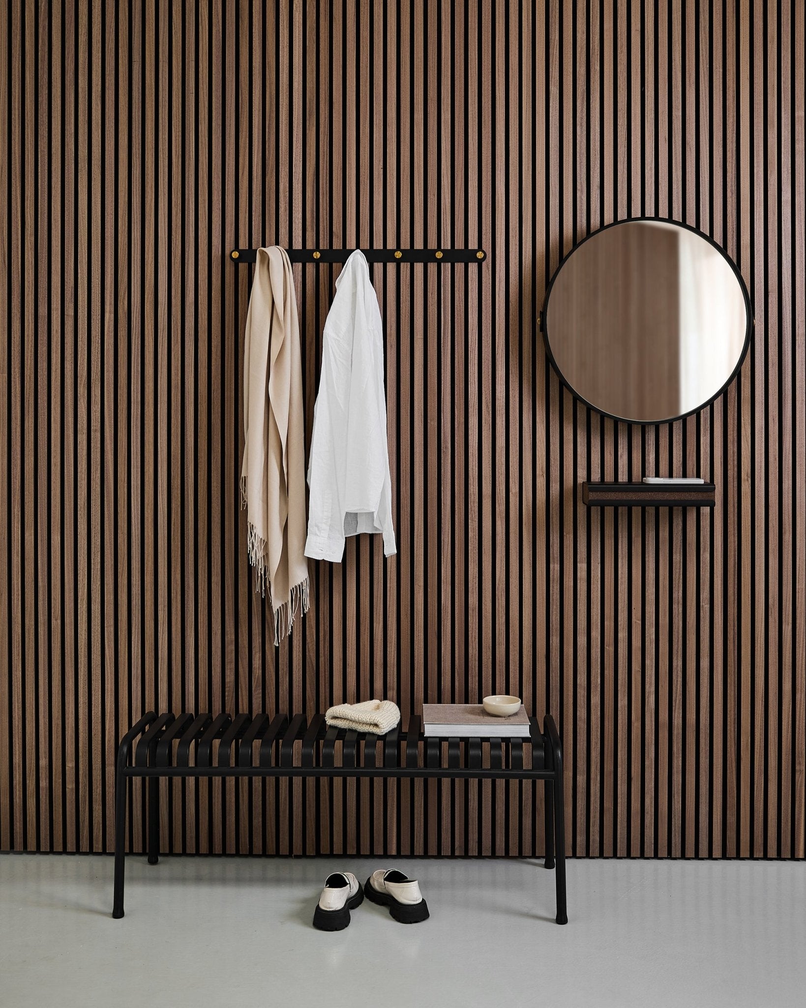 Minimalistische hal met een WoodUpp Linn | Mirror in Black Oak, een Scandinavisch akoestisch lattenwandpaneel, bankje, plank, opgehangen jas en sjaal, en schoenen op de vloer.