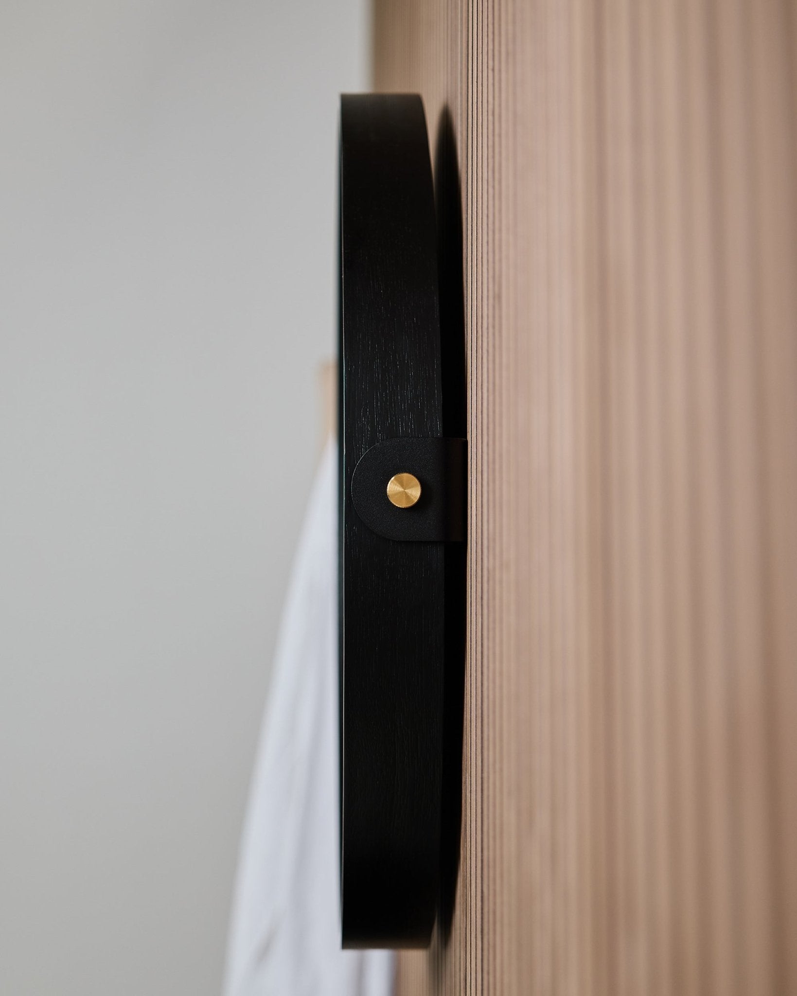 Close-up van de zijkant van de WoodUpp Linn | Mirror / Black Oak wandhaak, gemonteerd op een gegroefd eiken Akoestisch paneel, ontworpen om een ronde spiegel aan op te hangen.