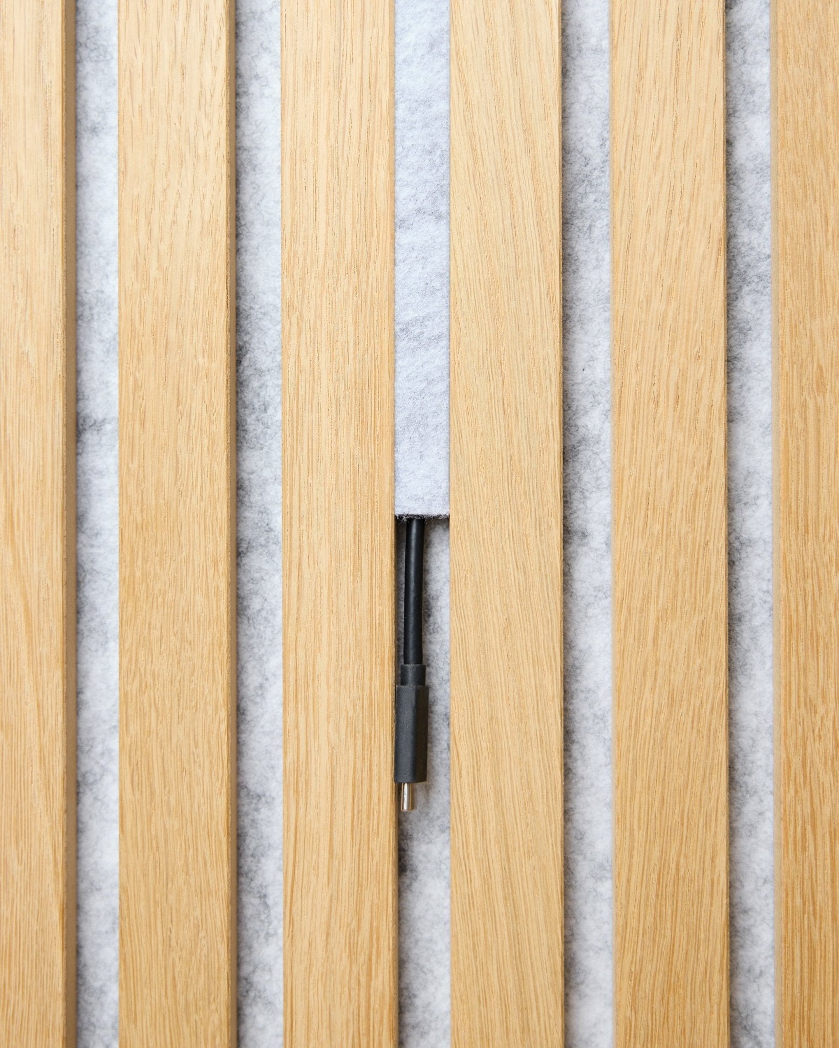 De Dupps Pop-on Cable Cover-set (grey, 3 stuks) van WoodUpp ordent kabels tussen lichtgekleurde houten Akupanel latten op een witte achtergrond met textuur.
