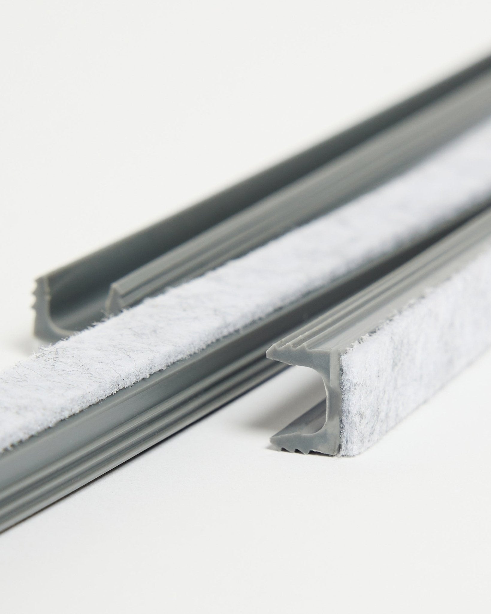 Drie grijze WoodUpp Dupps Pop-on Cable Covers met witte tochtstrip en flexibele TPV-kanalen liggen op een wit oppervlak.