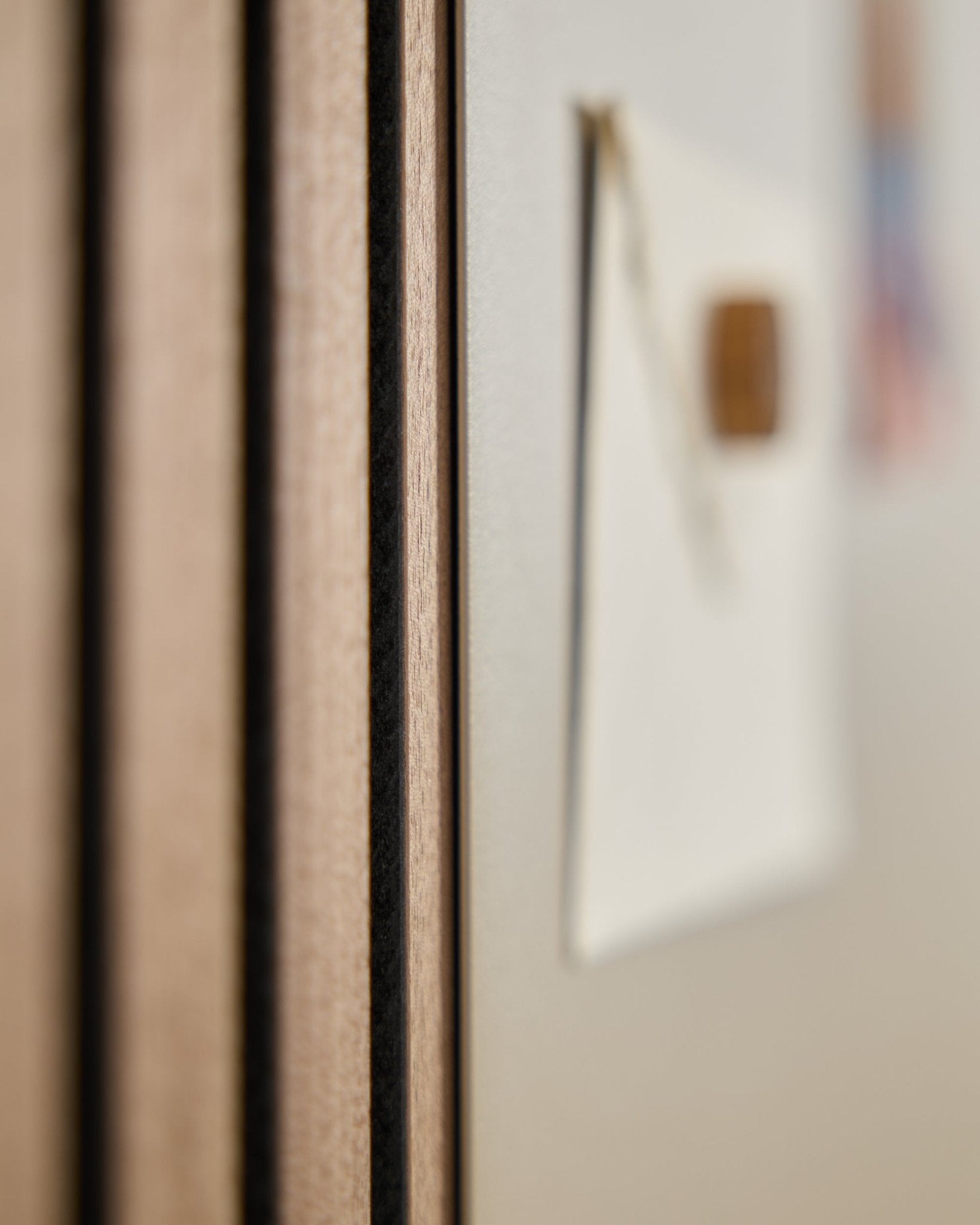Close-up van een WoodUpp Akupanel akoestisch houten paneel met vertical latten, naast een onscherp large beige Norr magneetbord op de achtergrond.