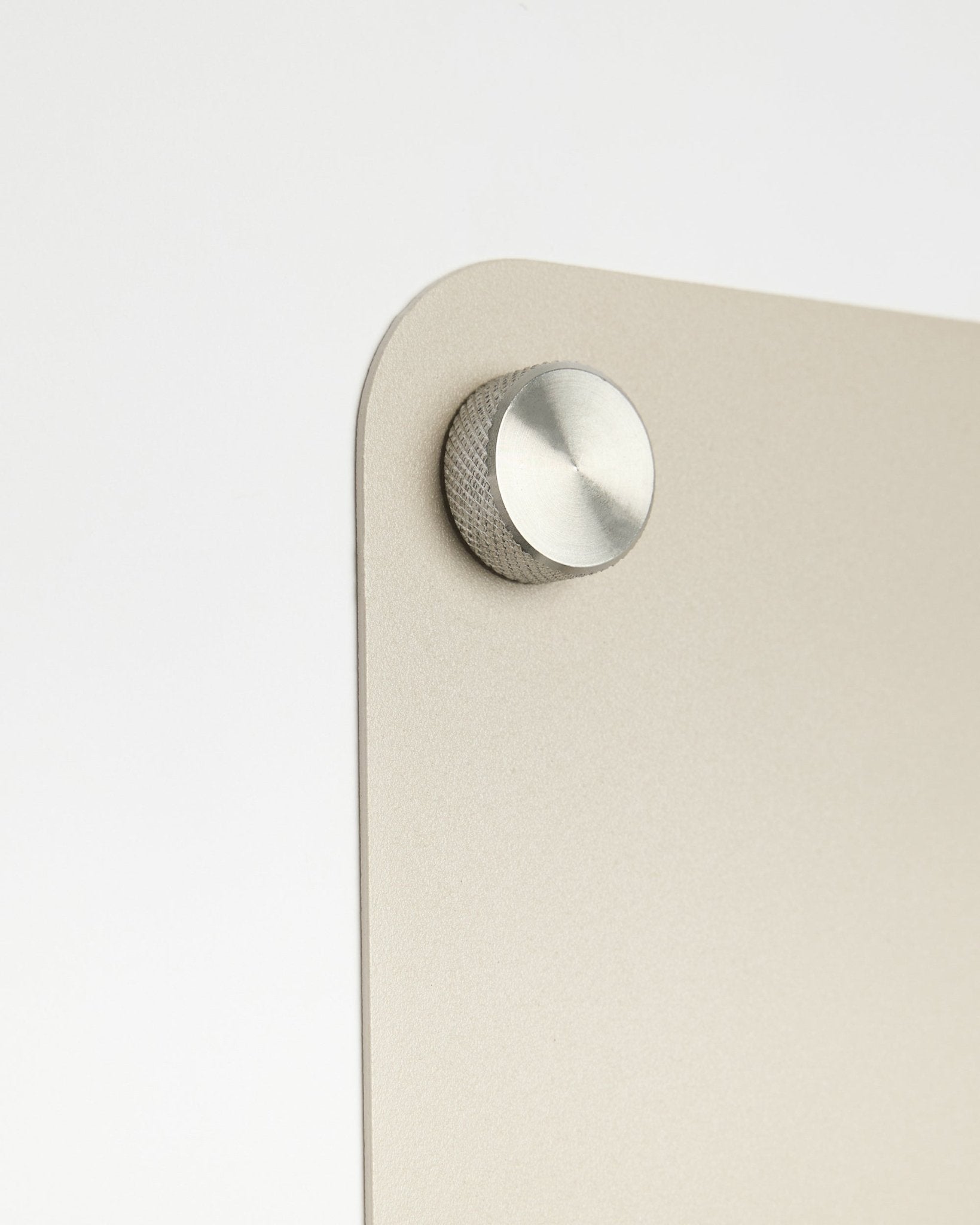 Close-up van een ronde metalen knopaccessoire bevestigd aan het large beige Norr magneetbord van WoodUpp, met een detail van matglas tegen een witte achtergrond.