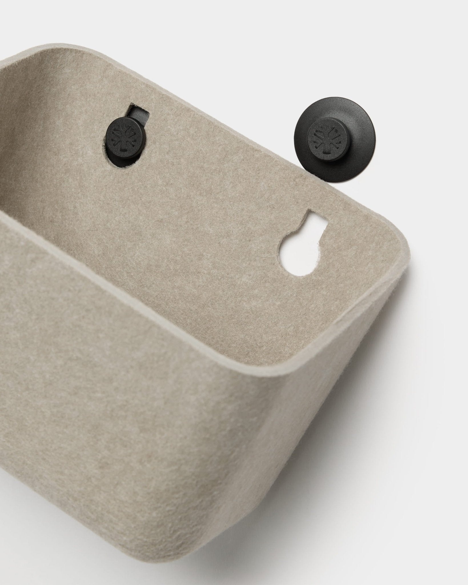 WoodUpp Luva beige vilten wandopbergaccessoire met twee zwarte ronde beugels; één beugel is los afgebeeld en naast de opbergbak geplaatst.