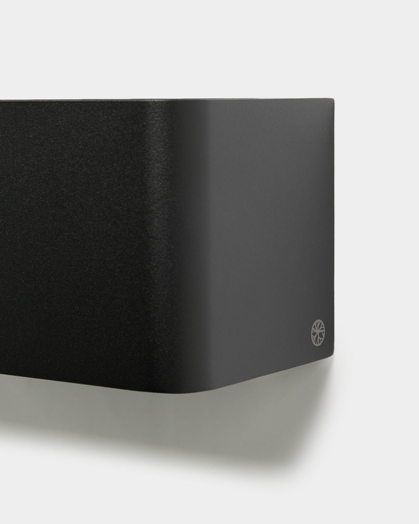 Close-up van de minimalistische WoodUpp Norr Plant Box (23.9 cm, black) met afgeronde randen en logo, gemonteerd op een witte muur. Scandinavisch akoestisch accessoireontwerp.