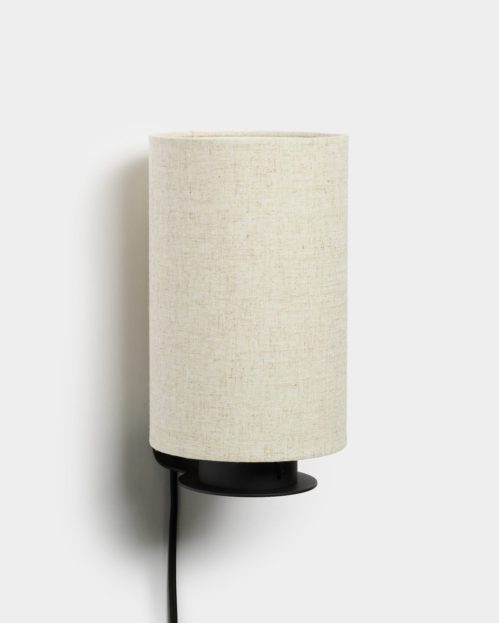 Feya wandlamp van WoodUpp met een metalen voet in black, een kap van linnen-katoen met textuur in beige en een zichtbaar netsnoer in black. Minimalistisch Scandinavisch design.