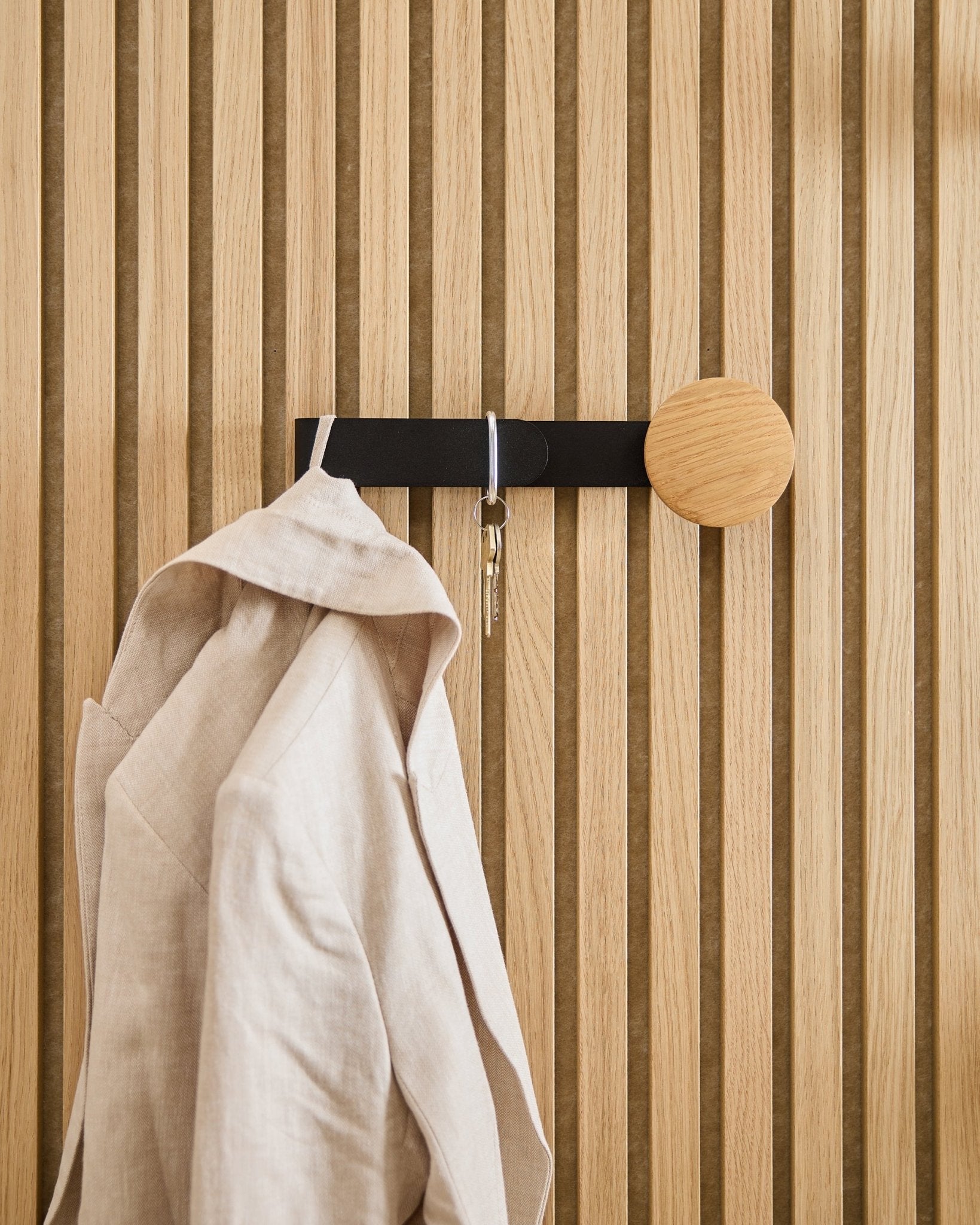 Een beige blazer en een set sleutels hangen aan de WoodUpp Linn Horizontal Hanger in natural oak, gemonteerd op een natural oak Akupanel akoestisch houten paneel.