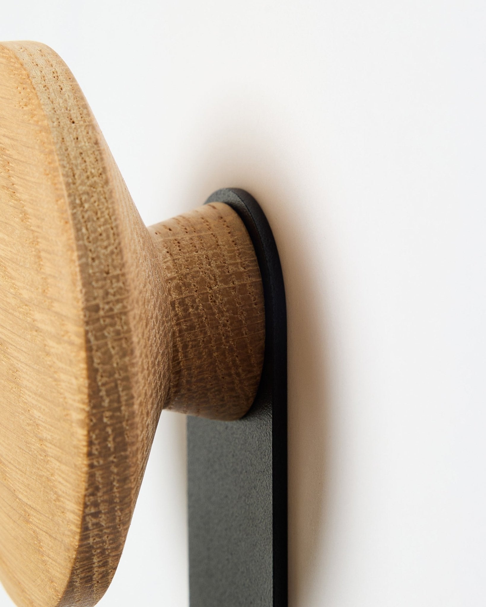 Close-up van de Linn Vertical Hanger in natural oak van WoodUpp, een accessoire met een ronde houten knop, gemonteerd op een beugel van black, ontworpen voor Akupanel akoestische panelen.