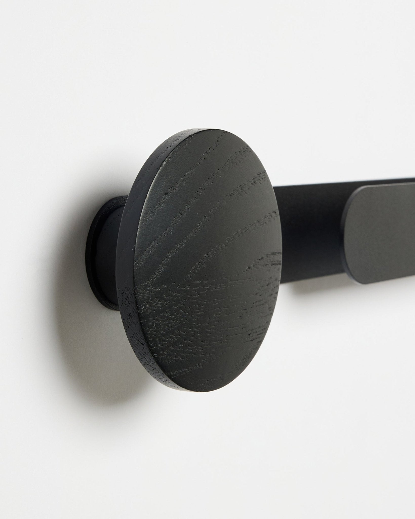 Close-up van de WoodUpp Linn | Horizontal Hanger in Black Oak, met een matte black afwerking, gemonteerd op een witte muur; accessoire voor akoestische houten panelen.