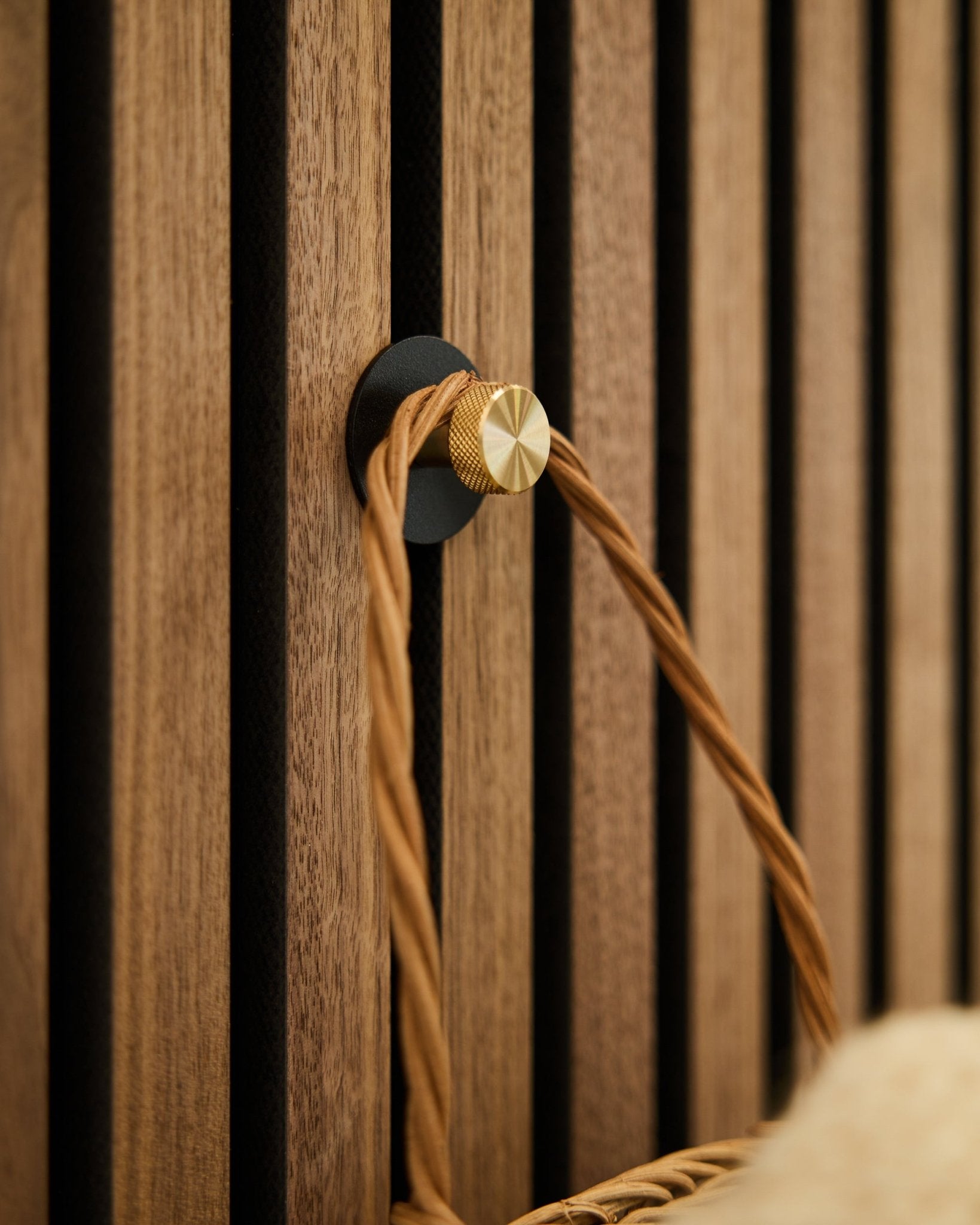 WoodUpp Norr kapstokhaak in black en brass, gemonteerd op een houten Akupanel Akoestisch paneel, houdt een lichtbruine gevlochten lus vast.