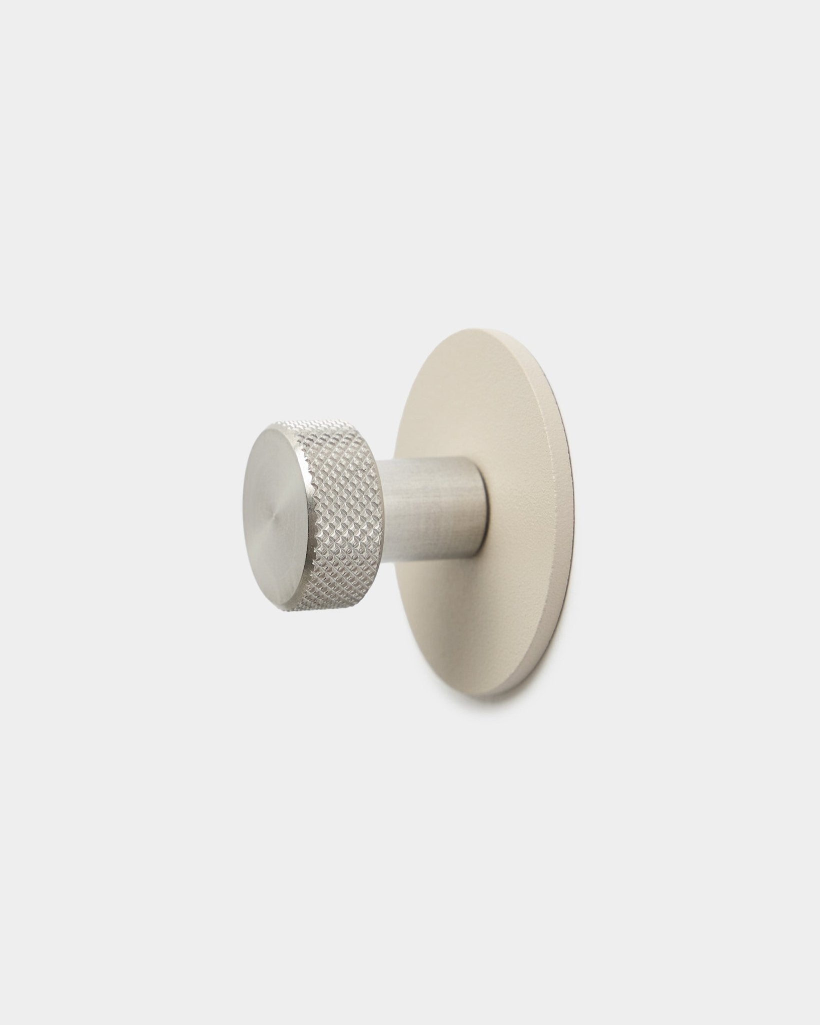 WoodUpp Norr kapstokhaak in beige en roestvrij steel met een cilindervormig uiteinde met textuur en ronde basis, accessoire voor Akupanel, op een effen witte achtergrond.