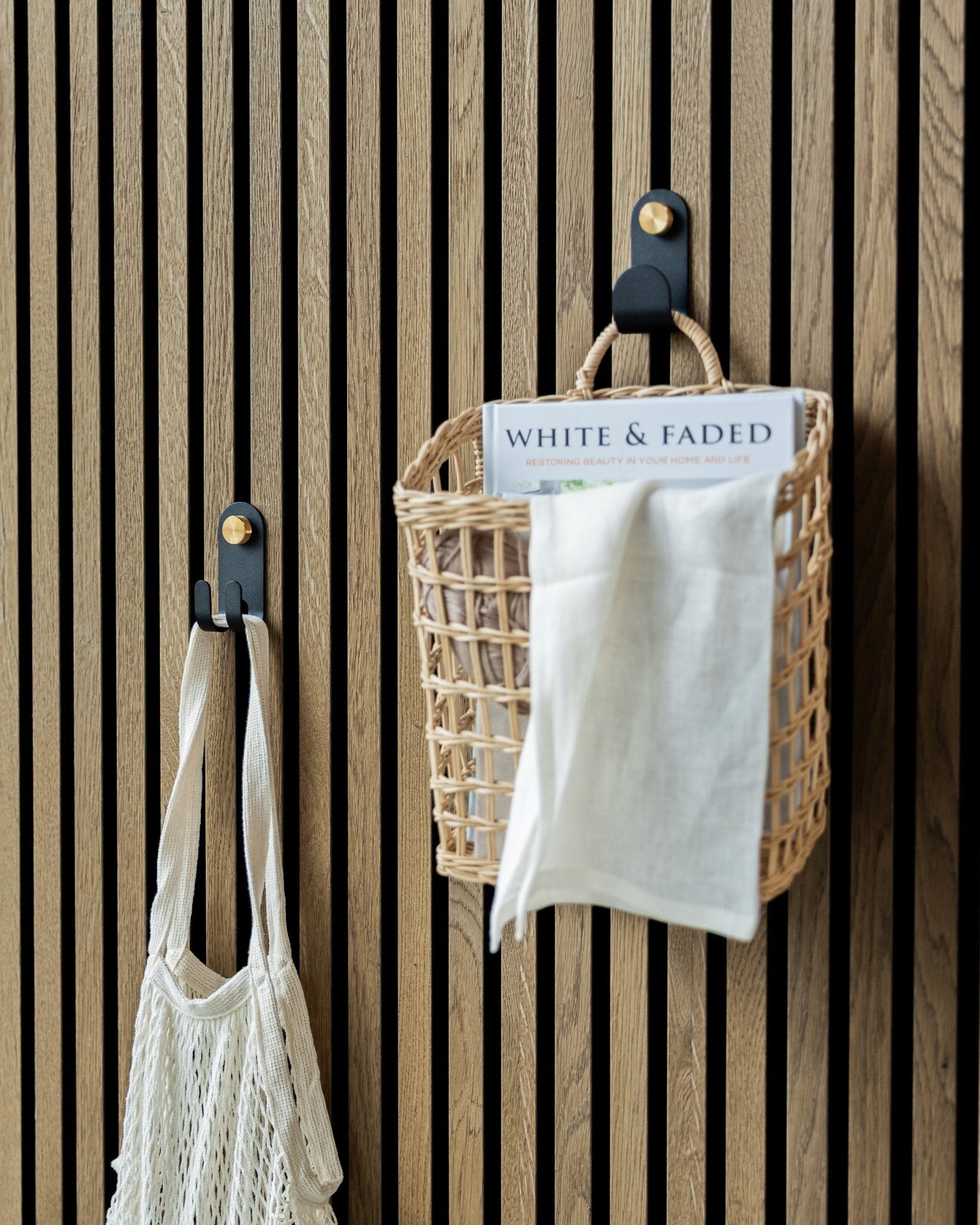 WoodUpp’s Norr Single Hanger in Black, met een geweven mand en netzak, gemonteerd op een Scandinavisch akoestisch lattenwandpaneel voor geordende opbergruimte.