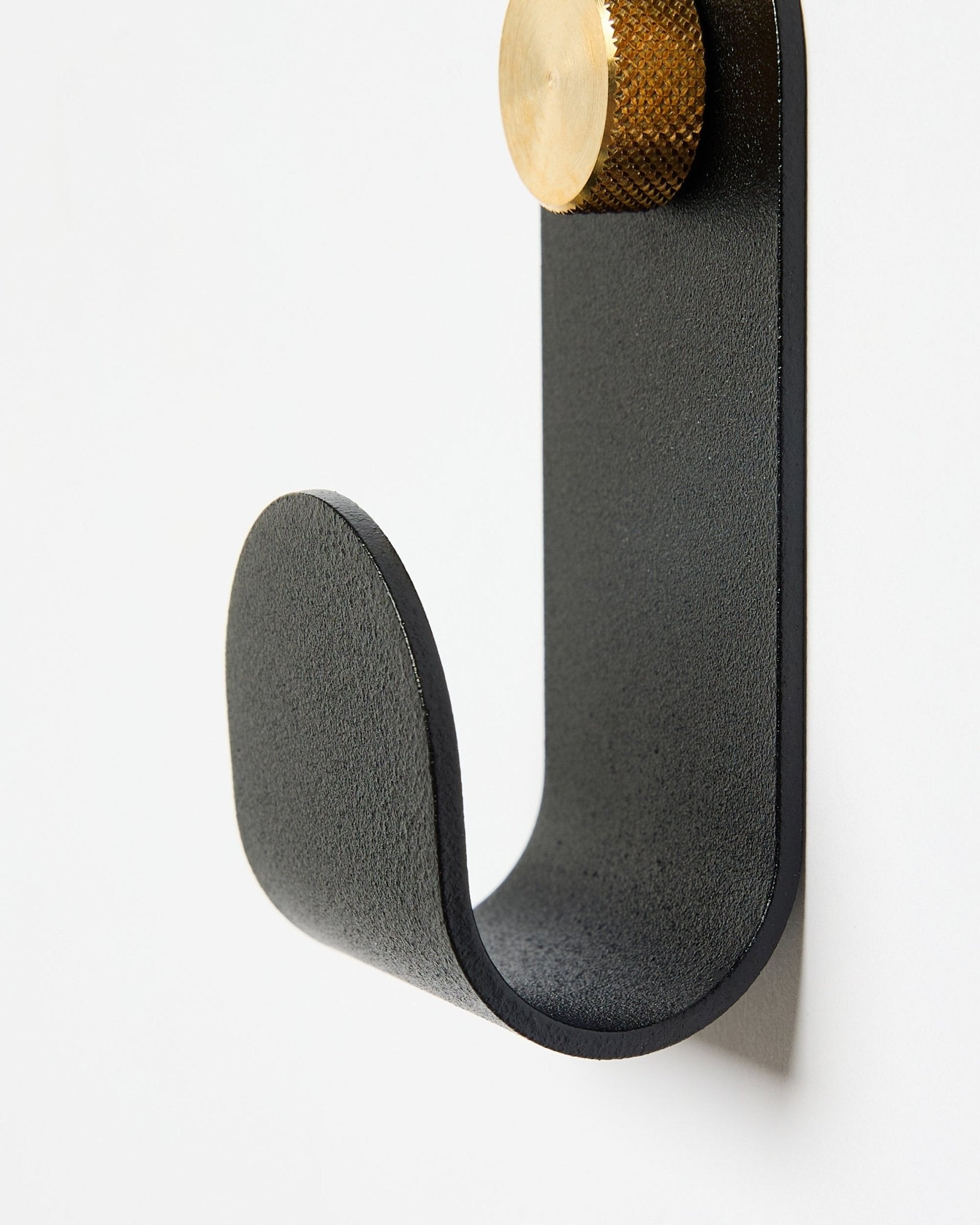 De Norr Single Hanger van WoodUpp heeft een gebogen arm van black met een gouden uiteinde, ontworpen als accessoire voor gebruik met akoestische panelen op witte muren.