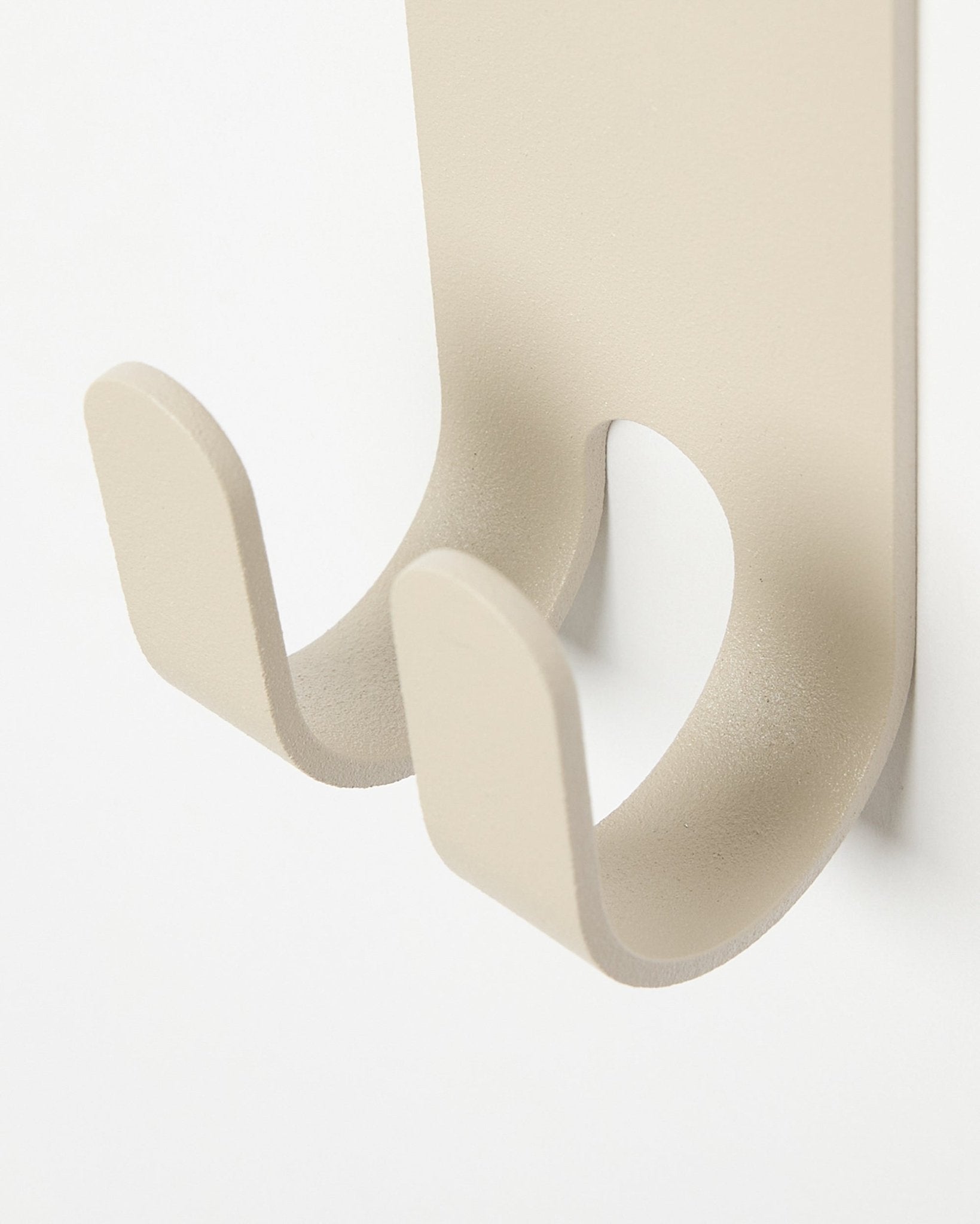 Close-up van de Norr Double Hanger in beige van WoodUpp, een minimalistische metalen kapstokhaak gemonteerd op een licht-colored Akoestisch paneel.