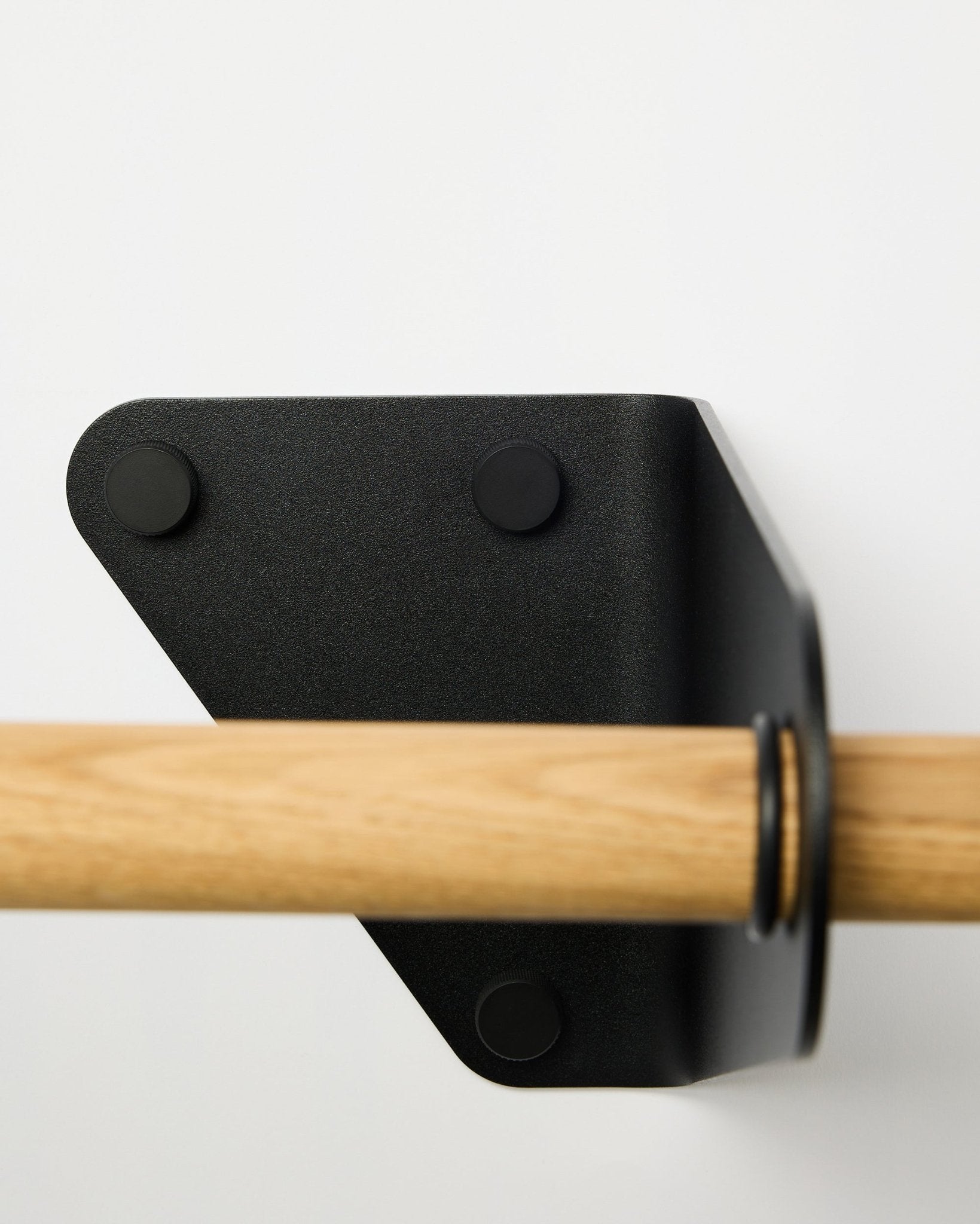 Close-up van de WoodUpp Linn kapstok in black, 115,9 cm, gemonteerd op een witte muur met een driehoekige metalen beugel, getoond als onderdeel van Nordic akoestische accessoires.
