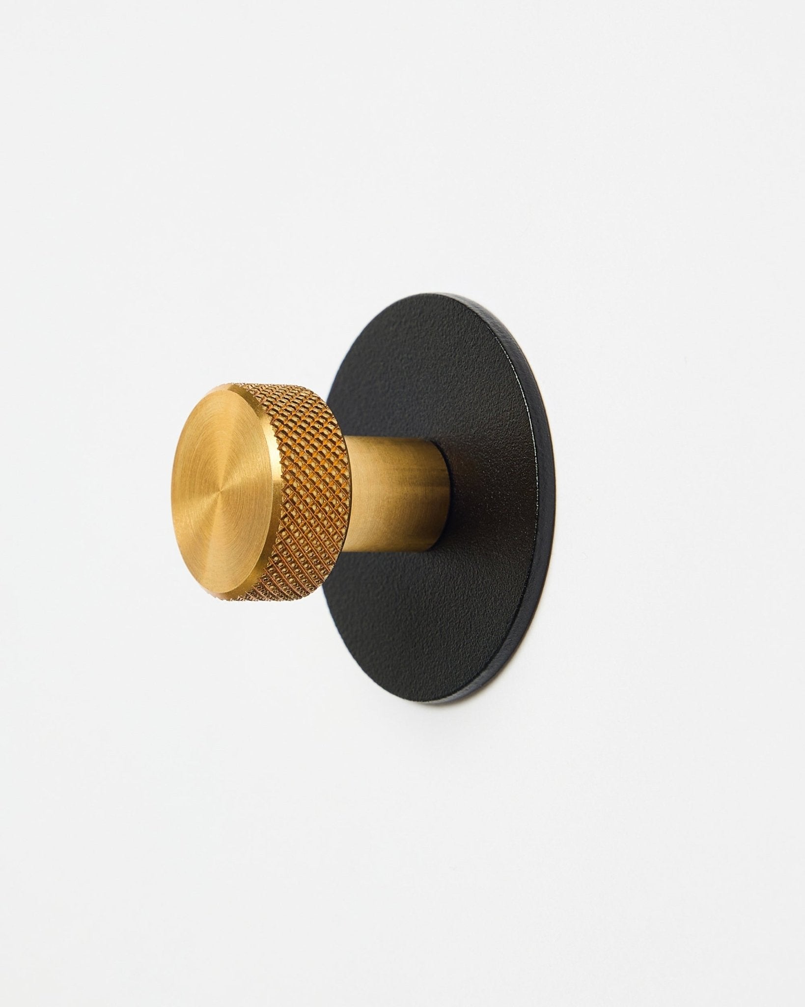 Norr Coat Hook X1 van WoodUpp met een knop met brass textuur en een black gepoedercoate steel basis, accessoire voor Akupanel, weergegeven op een witte achtergrond.
