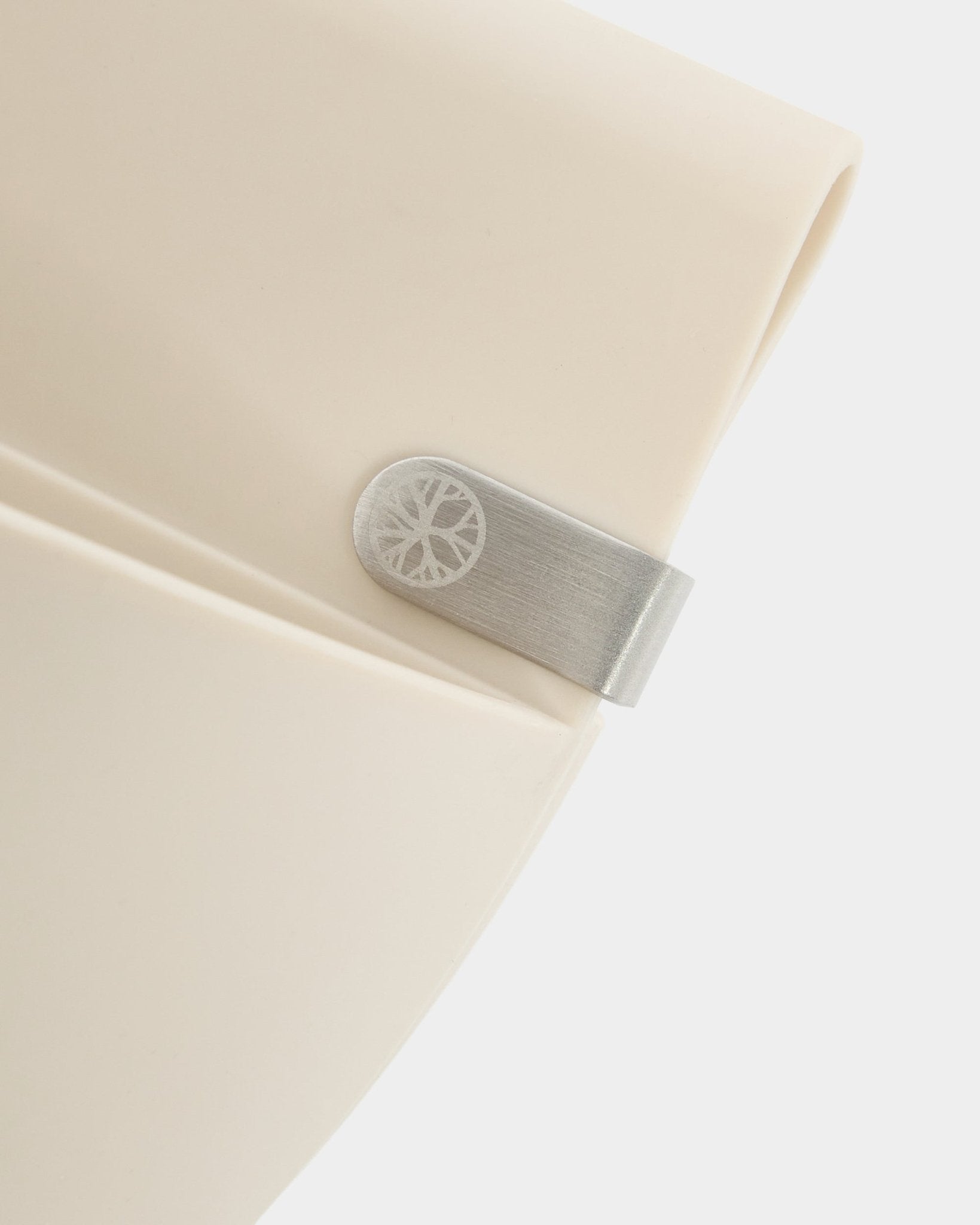Close-up van een licht beige WoodUpp Gro | Soft Pocket / BM2-paneel (4 l) met metalen clip en gegraveerd cirkeldetail op een effen witte achtergrond.