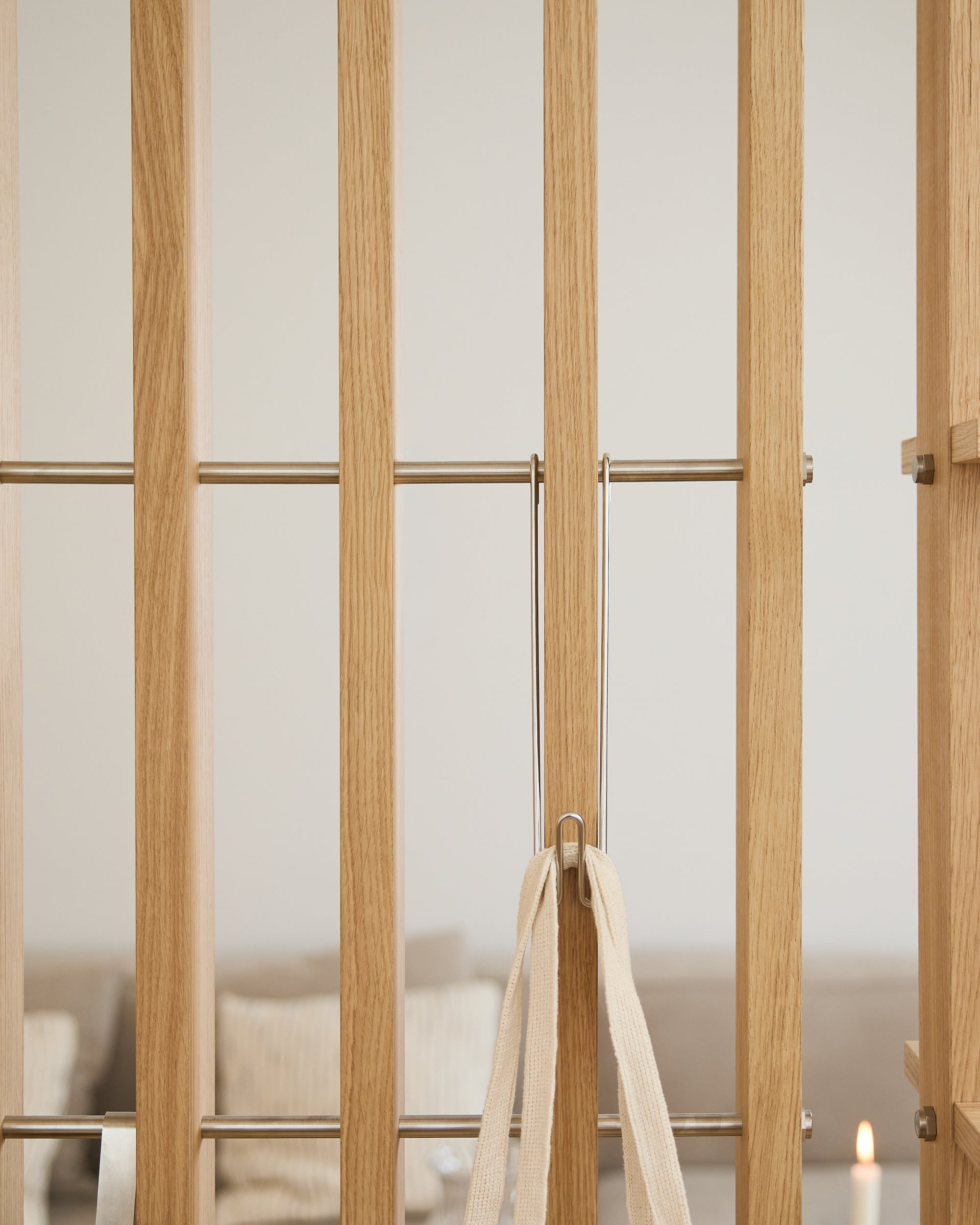 Lichte houten poort met metalen spijlen, een beige lint en drie WoodUpp Alva Wire Hooks/BM1; op de achtergrond een wazige bank en een kaars.