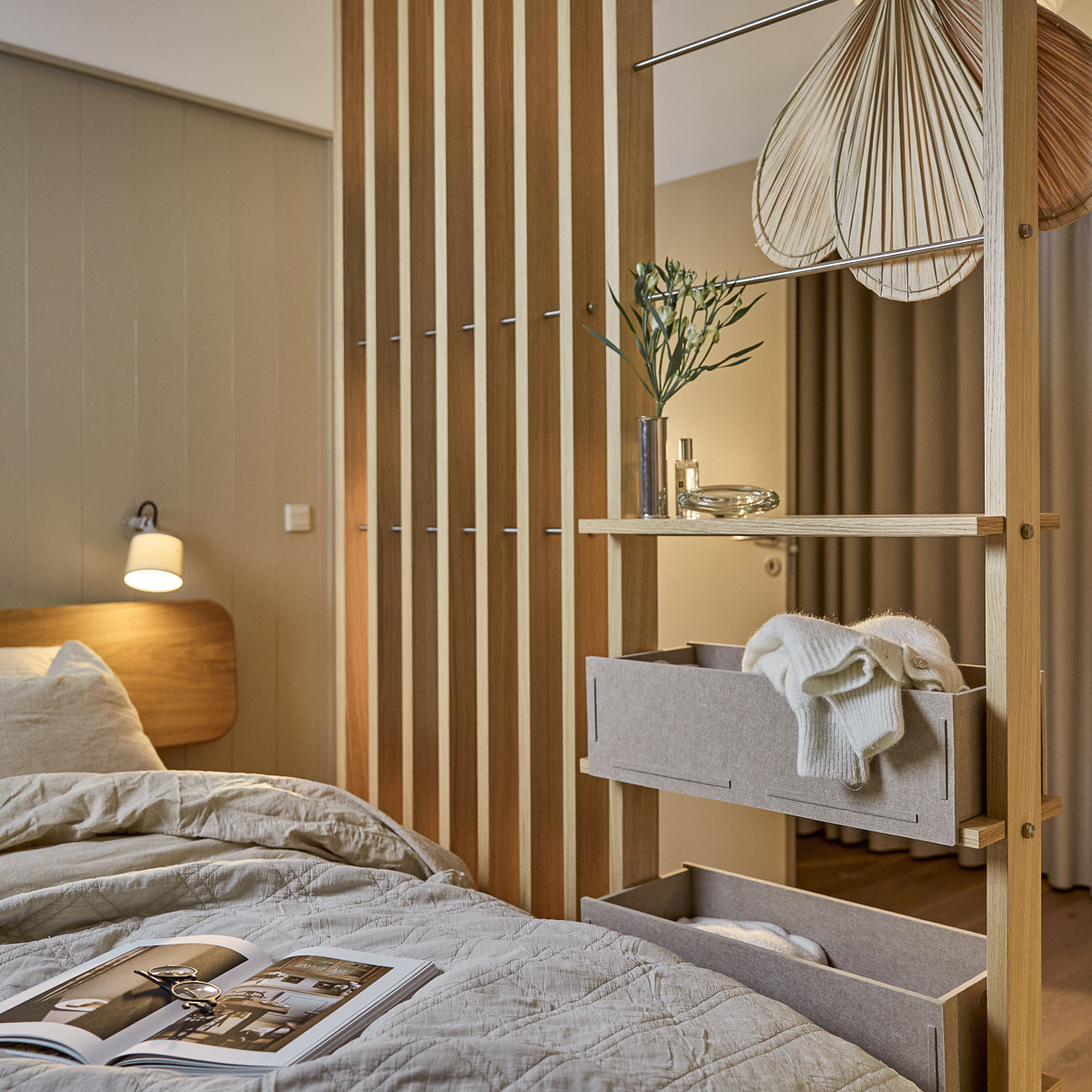 Een moderne slaapkamer met Scandinavisch zacht beddengoed, een hanglamp en een tijdschrift op het netjes opgemaakte bed. WoodUpp Akupanel akoestische houten panelen accentueren de muur.