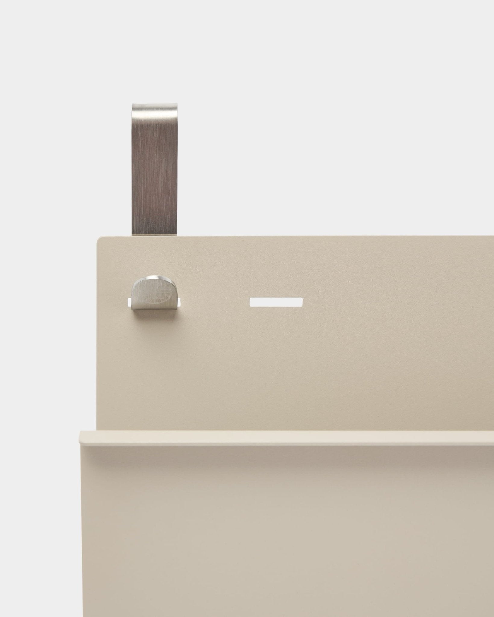 Close-up van WoodUpp Nell Magazine Storage in beige gepoedercoate steel met plank, sleuf, bout en gebogen handgreep; werkt als room divider of tijdschriftenhouder.