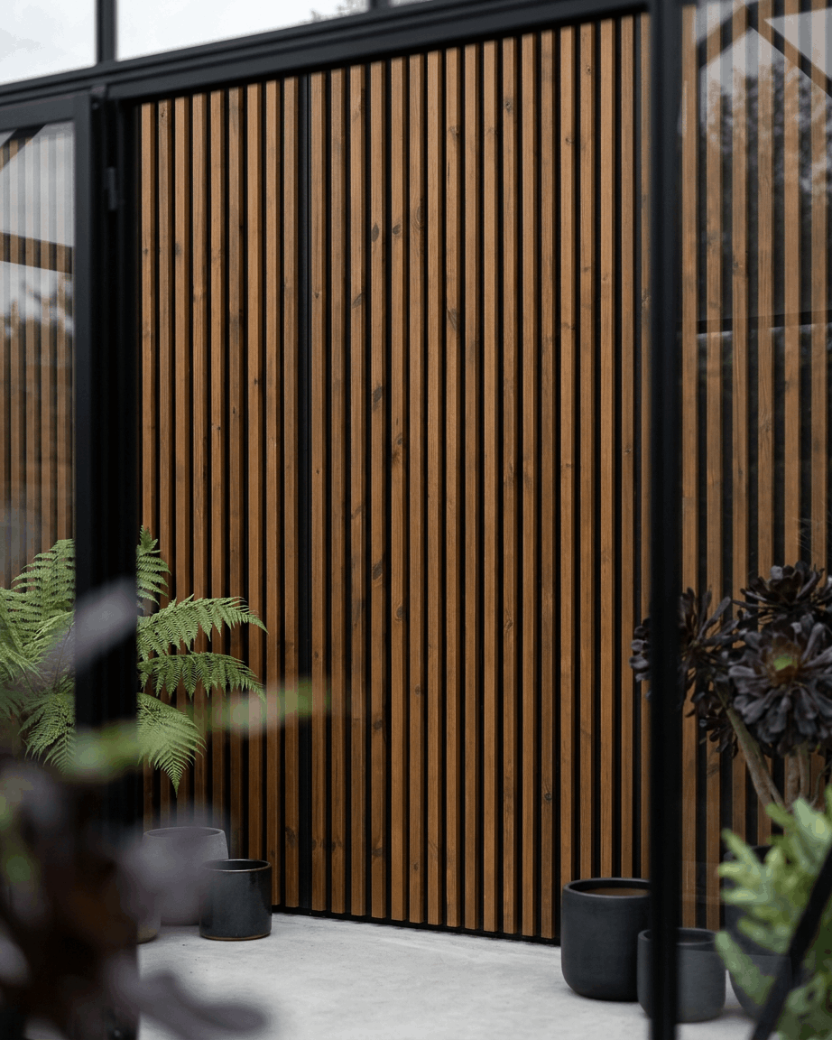 WoodUpp Aluwood-gevelpaneel voor buiten in geolied brown, gecombineerd met black plantenbakken en groene planten, voor een minimalistische Noordse patio.