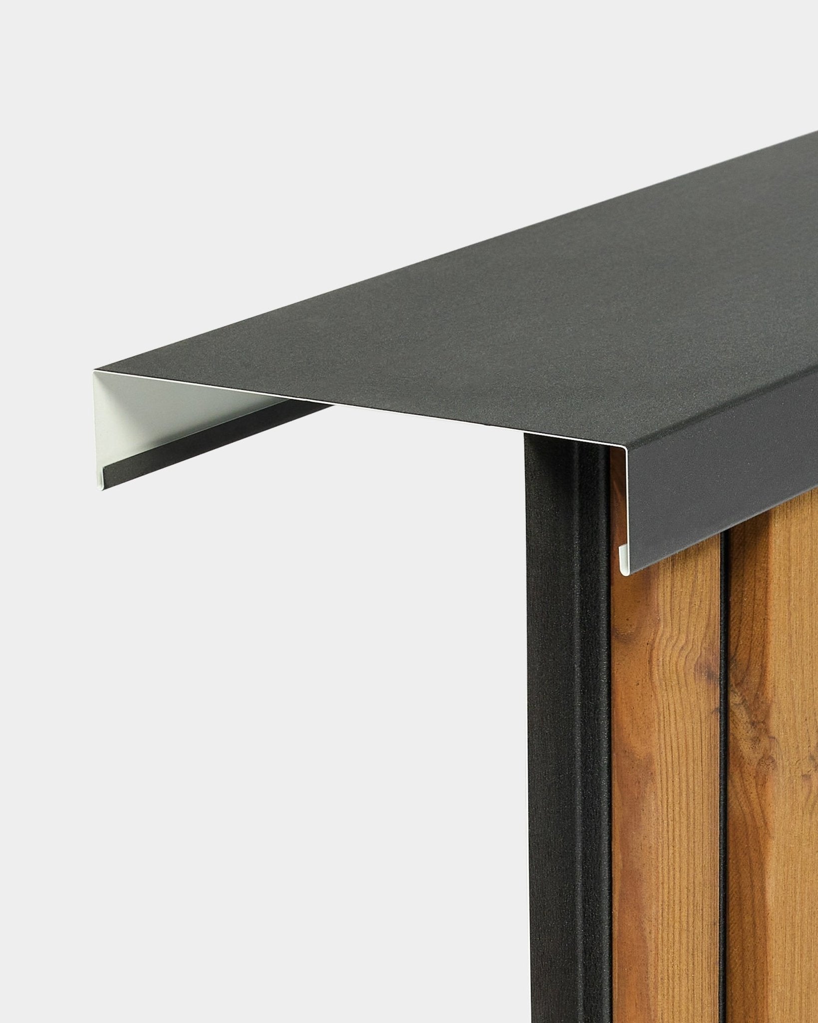 WoodUpp Aluwood Level wandafdekkap (240 cm x 20 cm) staat boven op een houten schutting, met een profiel van black gepoedercoat aluminium dat naar buiten uitsteekt.