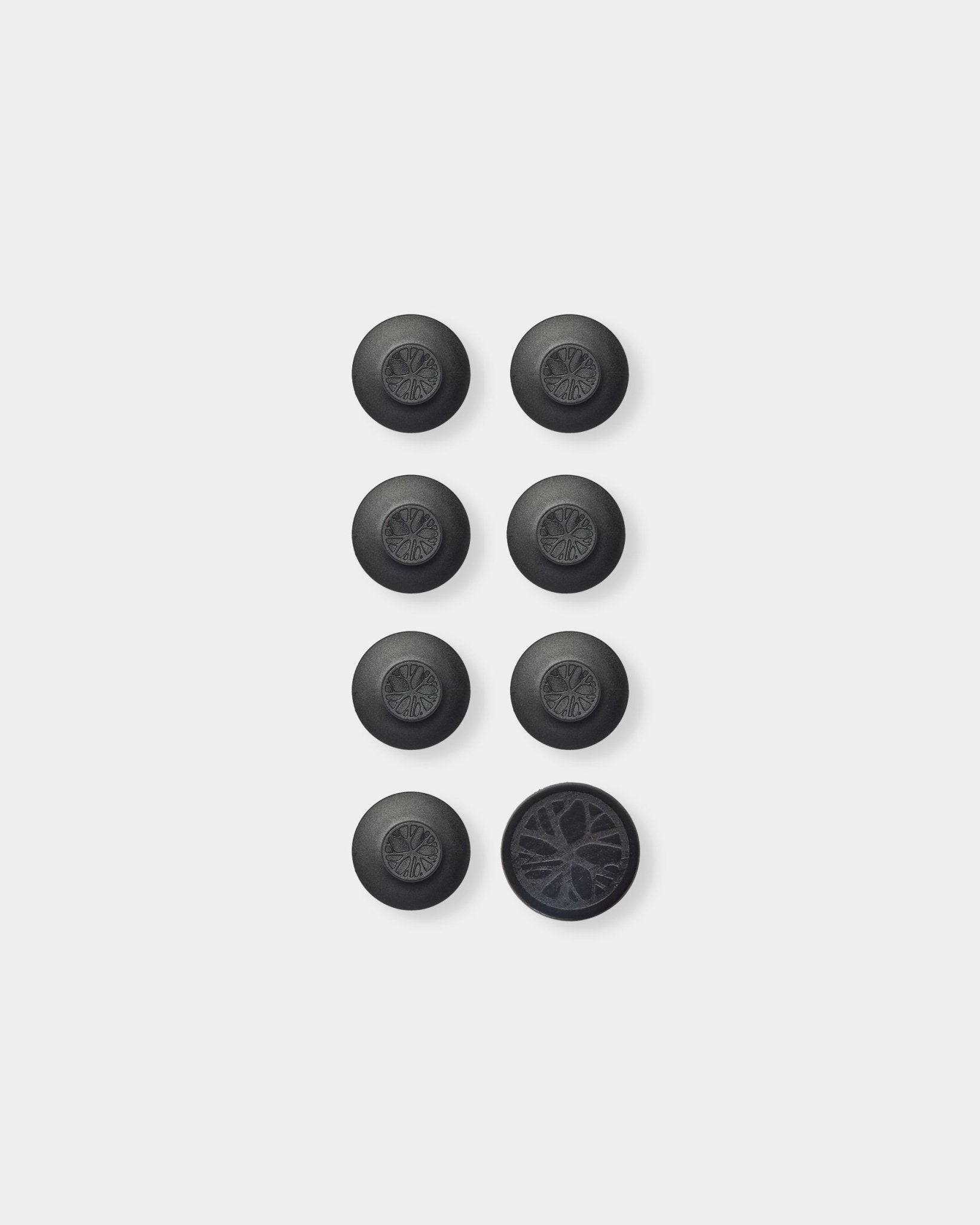 Zeven ronde black Dupps accessoires van WoodUpp en één tool, gerangschikt in een raster; rechtsonder is de Dupp omgedraaid zodat de onderzijde met textuur zichtbaar is.