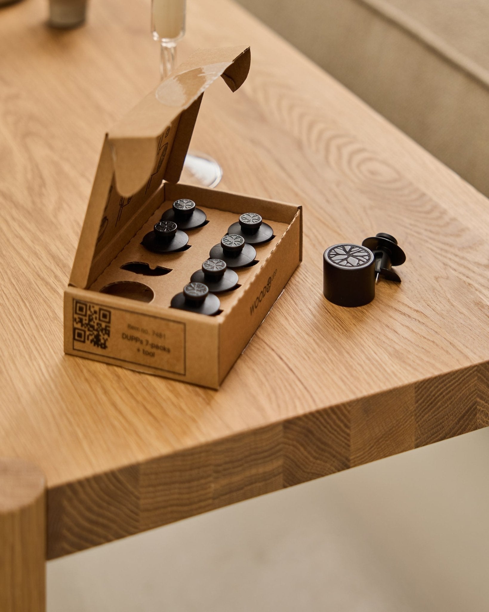De WoodUpp Dupps Original set (7 stuks en 1 tool), gerangschikt op een houten tafel, met aan de rand één Dupps onderdeel en een deel van een glas in beeld.