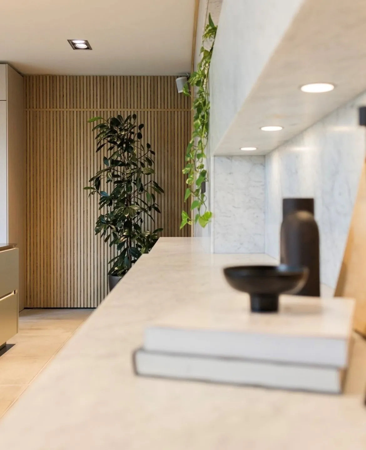Een modern interieur met een marmeren plank, decoratieve objecten, groene planten en een Scandinavische akoestische houten wand van Akupanel op de achtergrond.