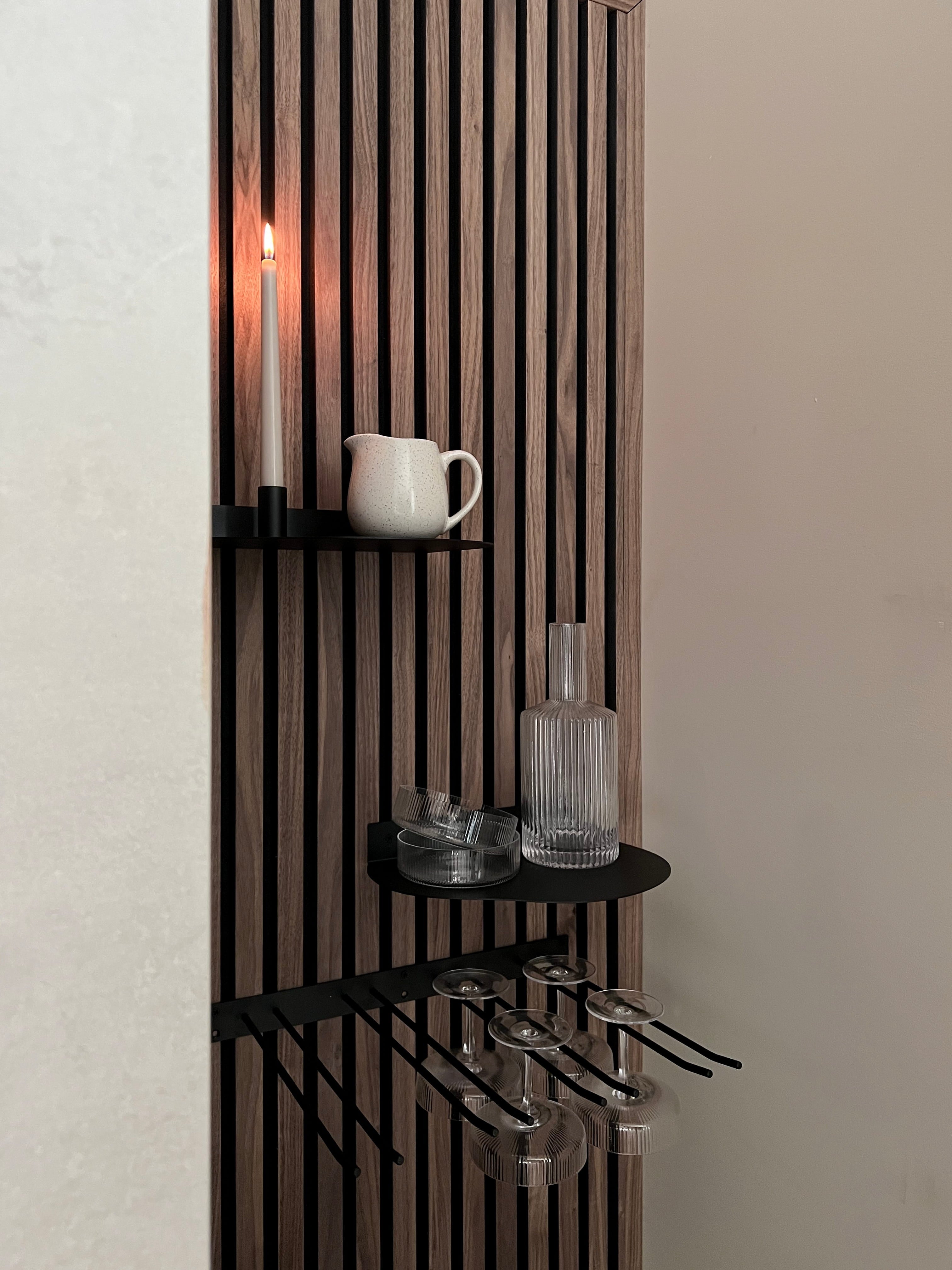 Modern Scandinavisch akoestisch lamellenpaneel met zwarte planken met daarop een brandende kaars, witte kan, glazen fles en wijnglazen met steeltjes.