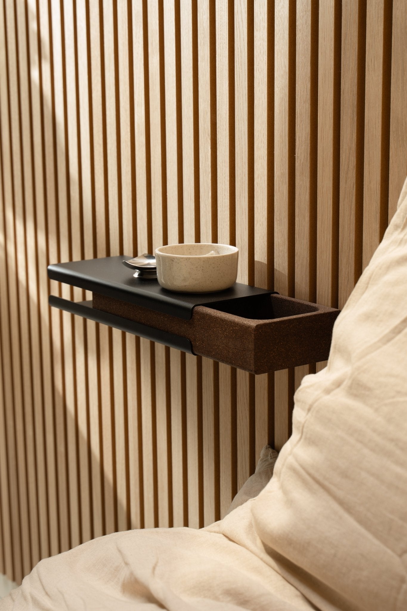 Minimalistische wandplank met een keramische schaal en WoodUpp Norr Key Tray naast een beige kussen en Akupanel Akoestisch paneel, verlicht door zacht natuurlijk licht.